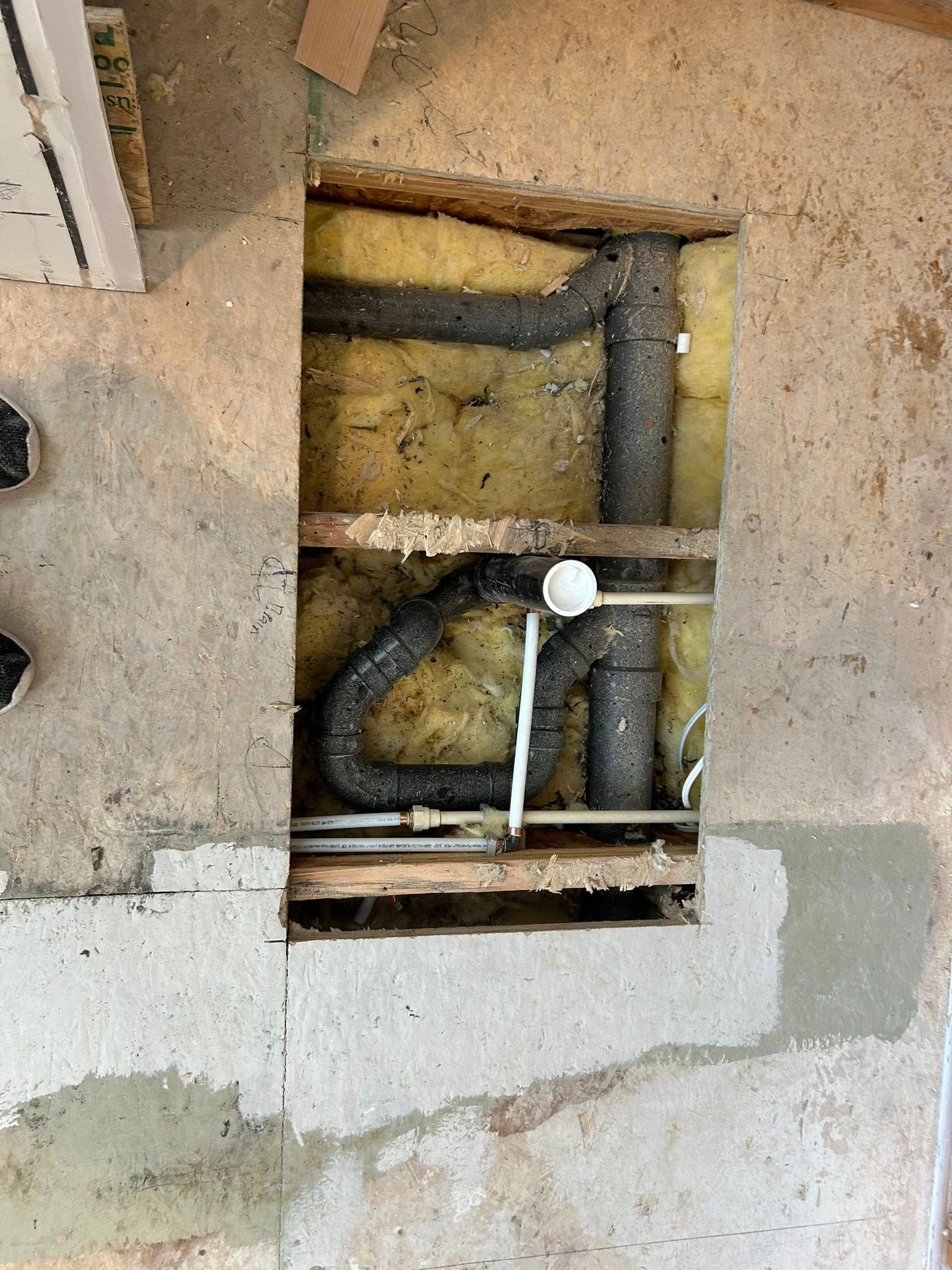 Plumbing pipes within a rectangular opening in a concrete floor, with yellow insulation visible.