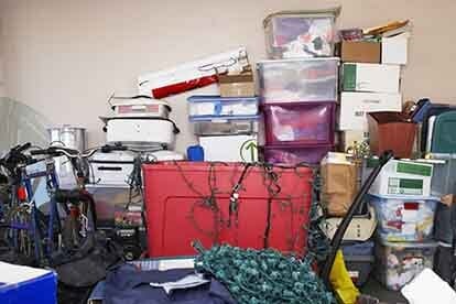 A cluttered storage area with boxes, bins, and various items piled against a wall.