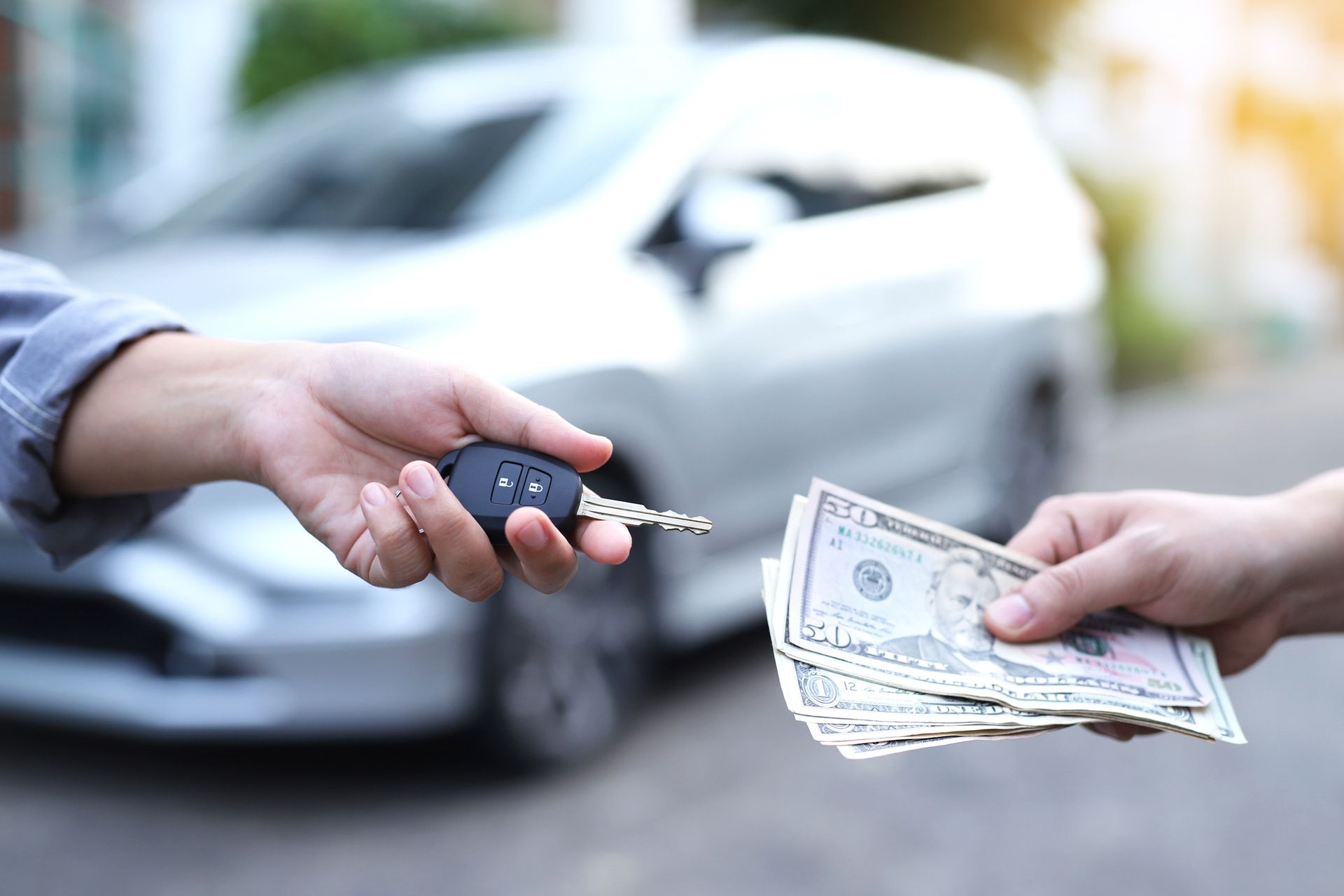 Sell my car for cash – Person handing over car keys in exchange for cash in front of a gray vehicle. 
