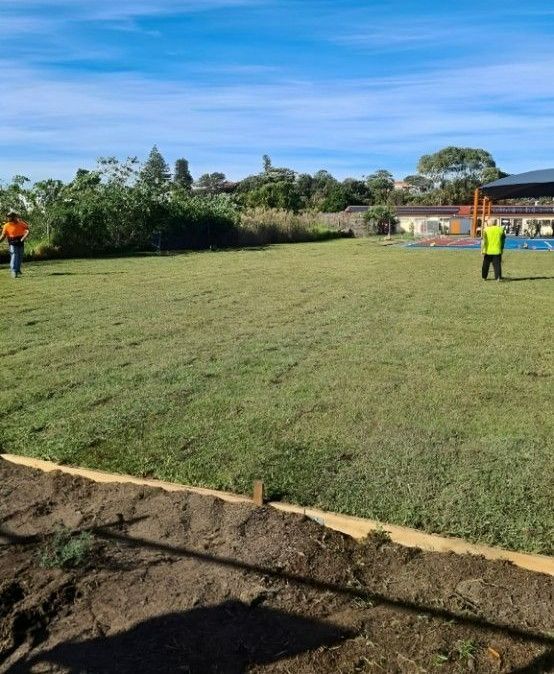 A Man in a Yellow Vest is Standing in the Middle of a Lush Green Field — Superior Turf in Oak Flats, NSW