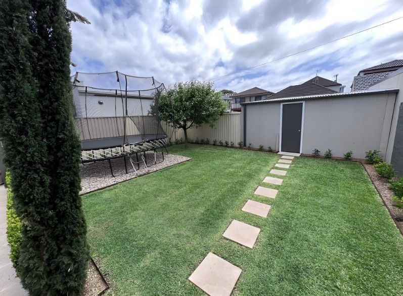 A Lush Green Backyard With a Stone Walkway Leading to a Shed — Superior Turf in Oak Flats, NSW