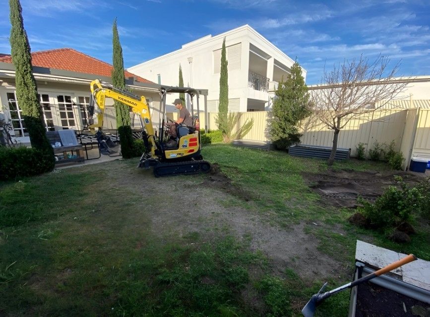 A Man is Driving a Small Excavator in a Backyard — Superior Turf in Tullimbar, NSW