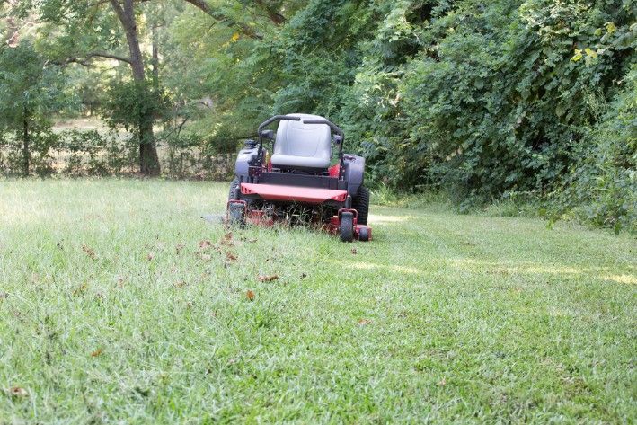 A Person is Mowing a Lush Green Lawn With a Lawn Mower — Superior Turf in Shoalhaven, NSW
