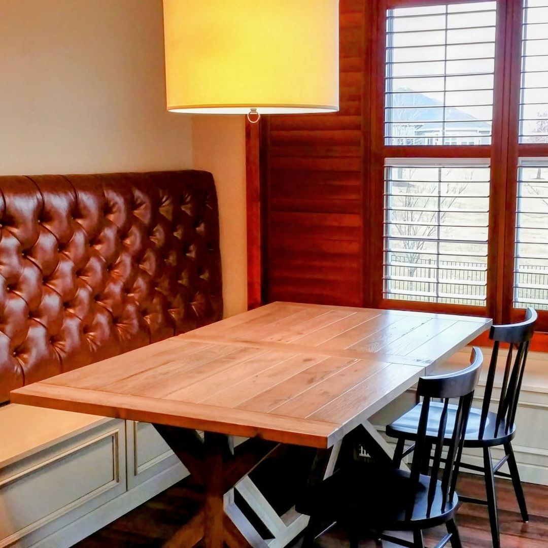 Dining nook with a leather tufted bench, wooden table, and two black chairs near a window.