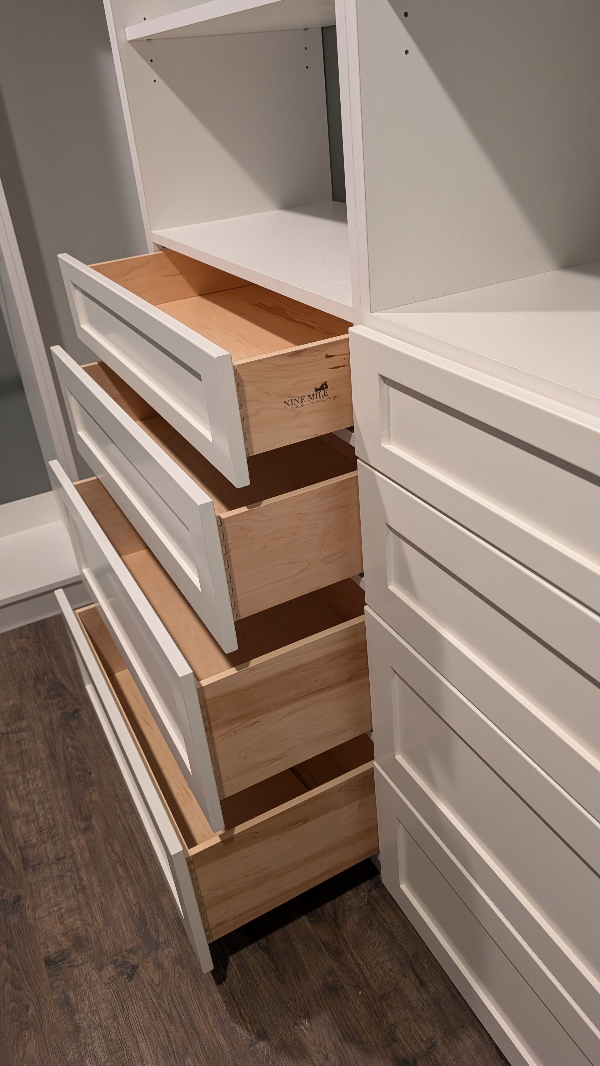 A closet with white drawers and wooden drawers.