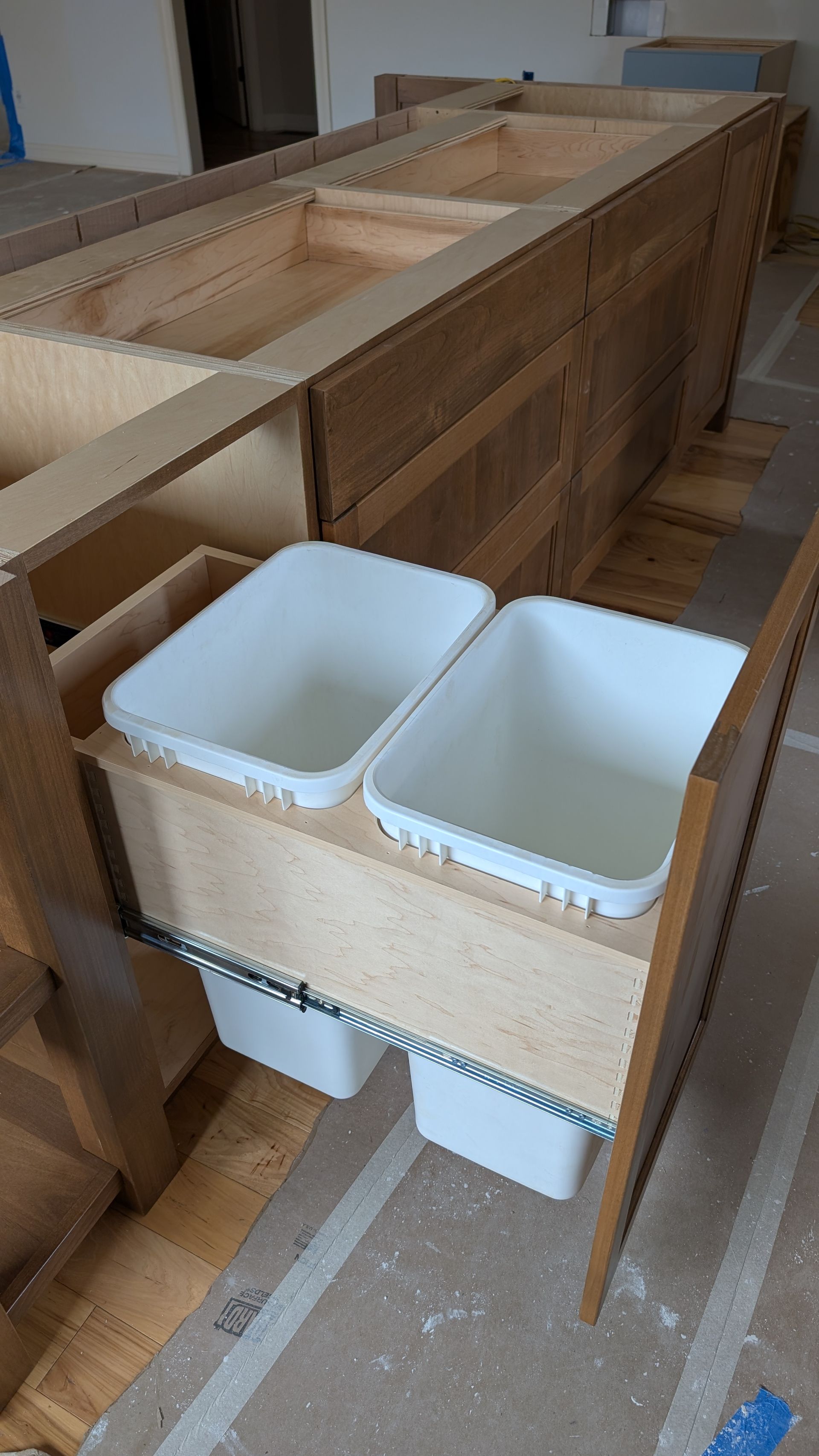 Two white trash cans are pulled out of a wooden cabinet.