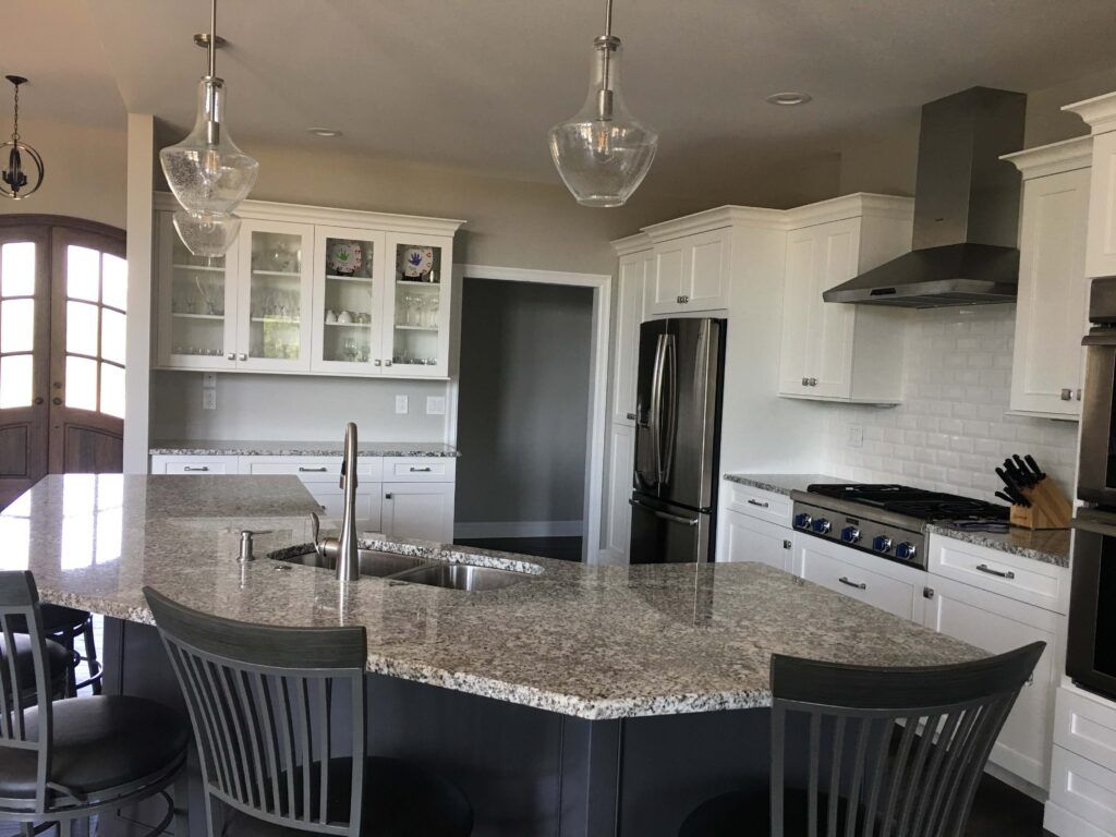 A kitchen with white cabinets , granite counter tops , stainless steel appliances and a large island.