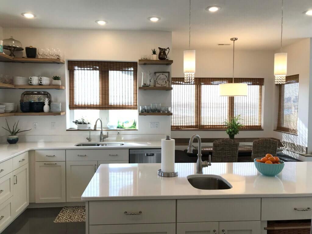 A kitchen with white cabinets , a sink , and a bowl of oranges on the counter.
