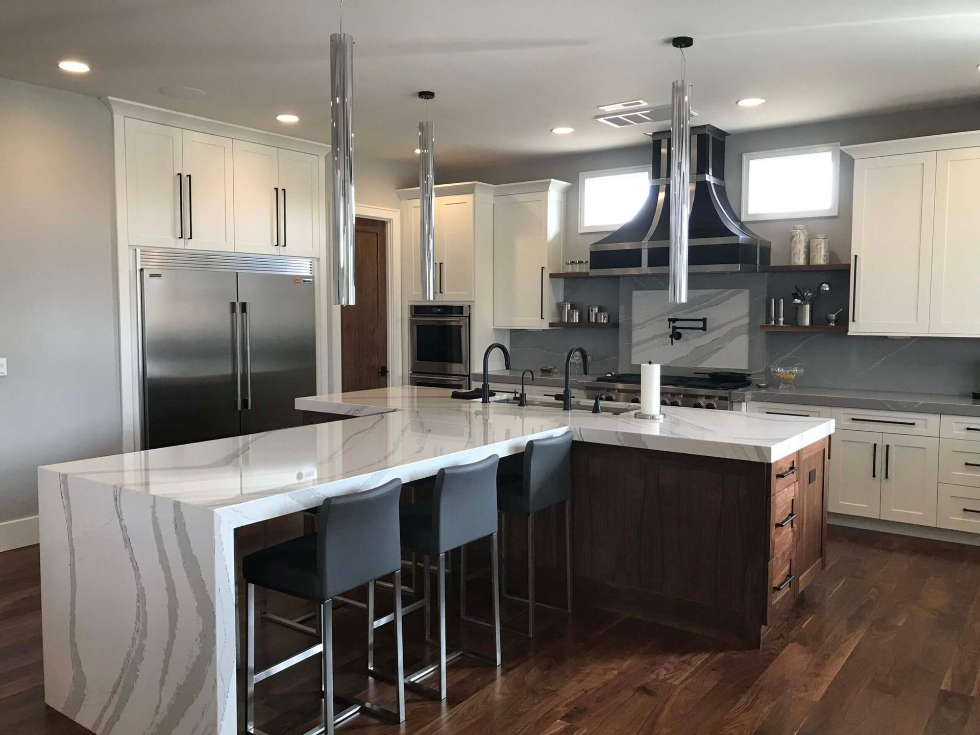 A kitchen with a large island , stainless steel appliances , white cabinets and hardwood floors.