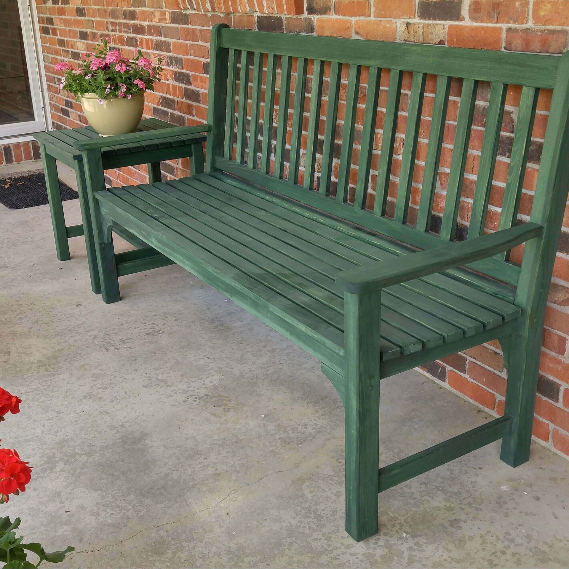 A green bench sits on a porch next to a small table