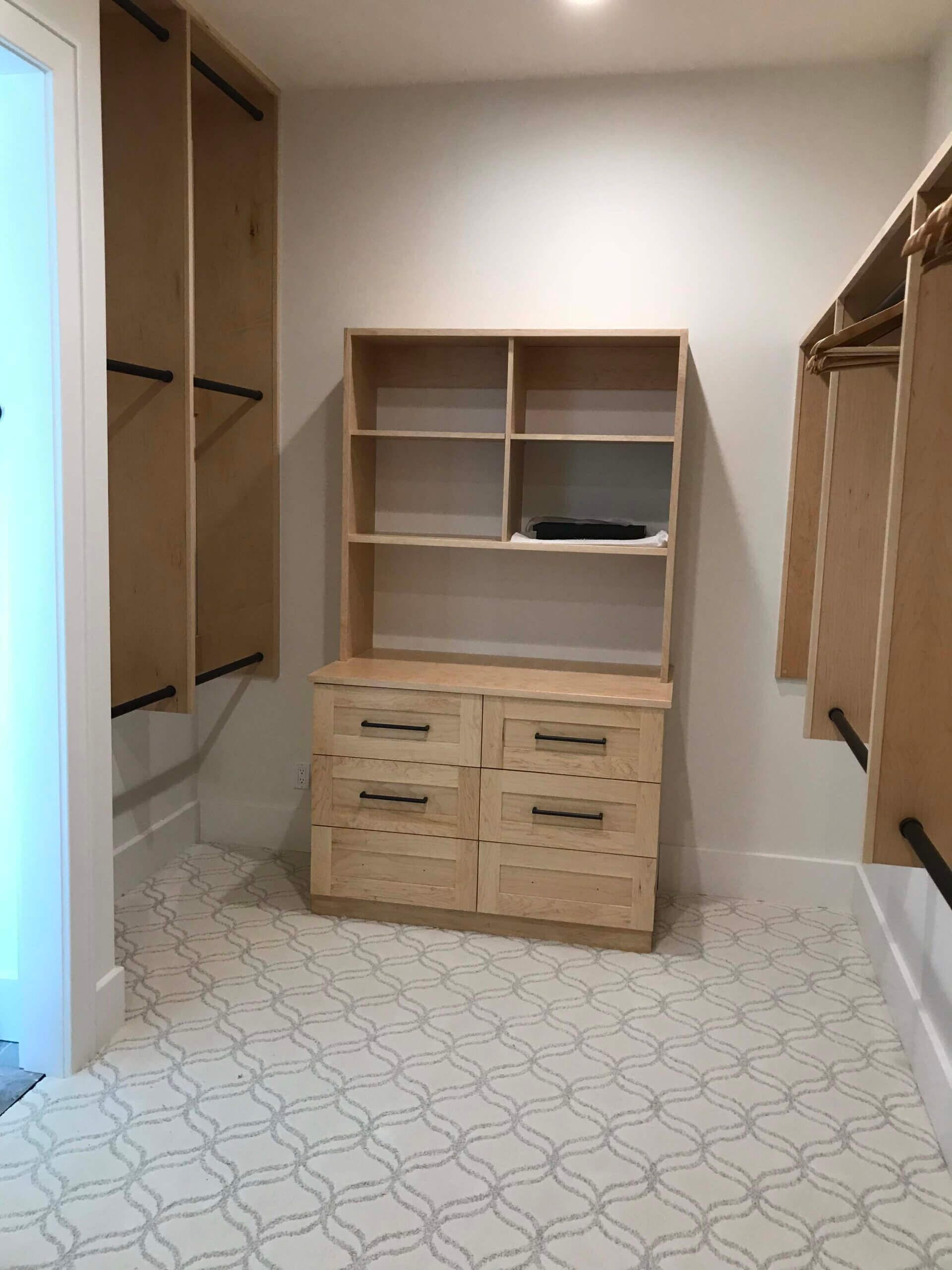A walk in closet with a wooden dresser and shelves.