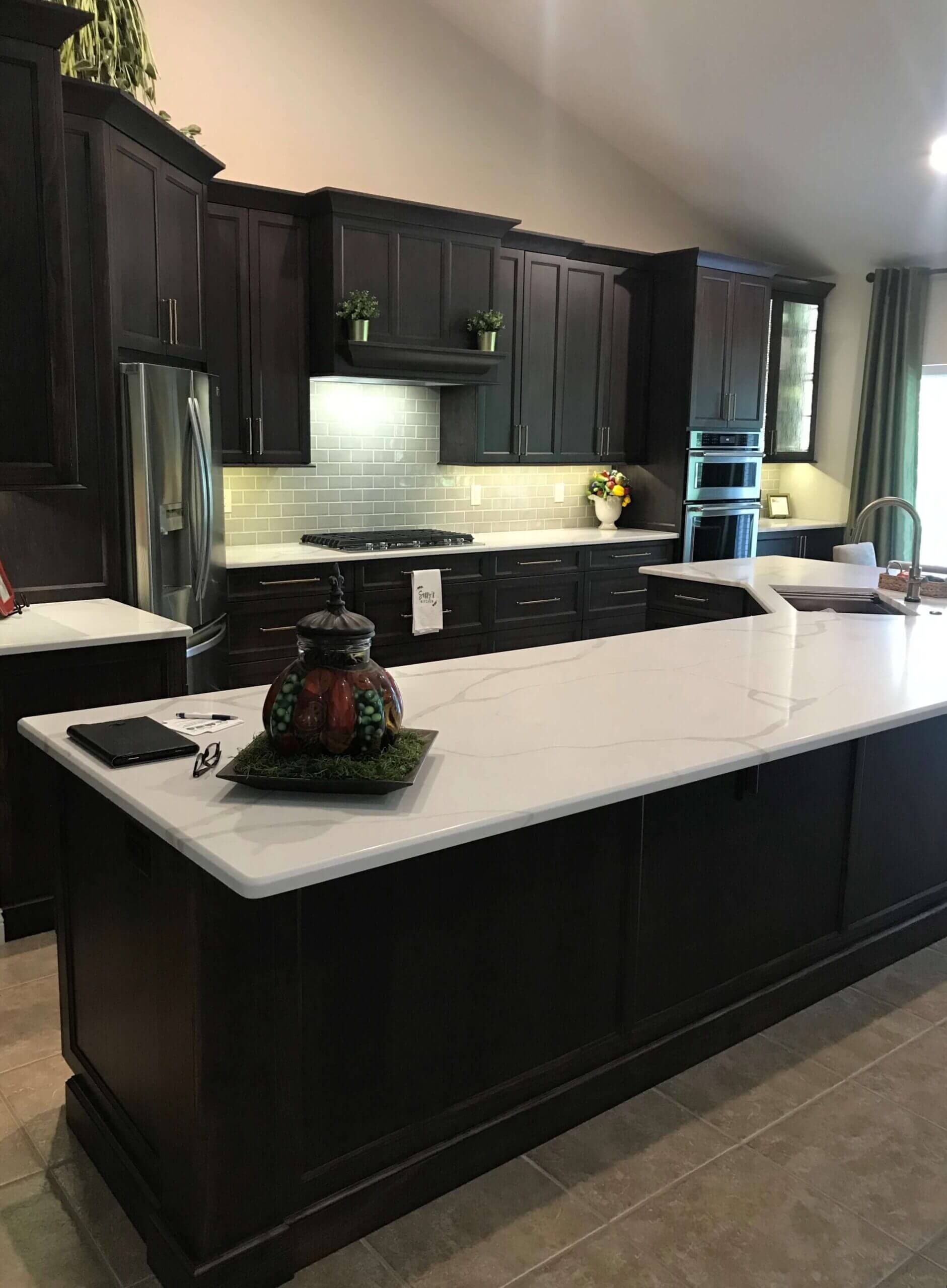 A kitchen with black cabinets and white counter tops and a large island.