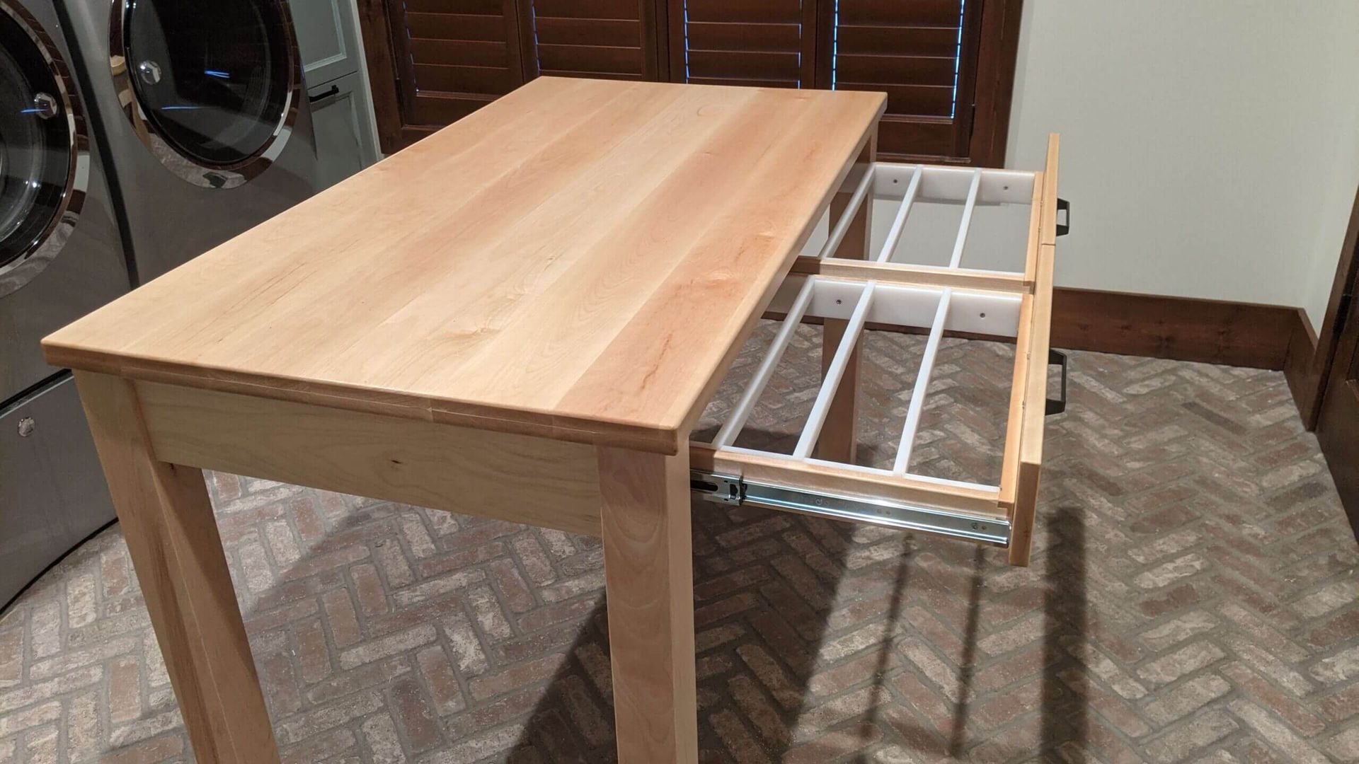 A wooden table with a drawer underneath it in a laundry room.