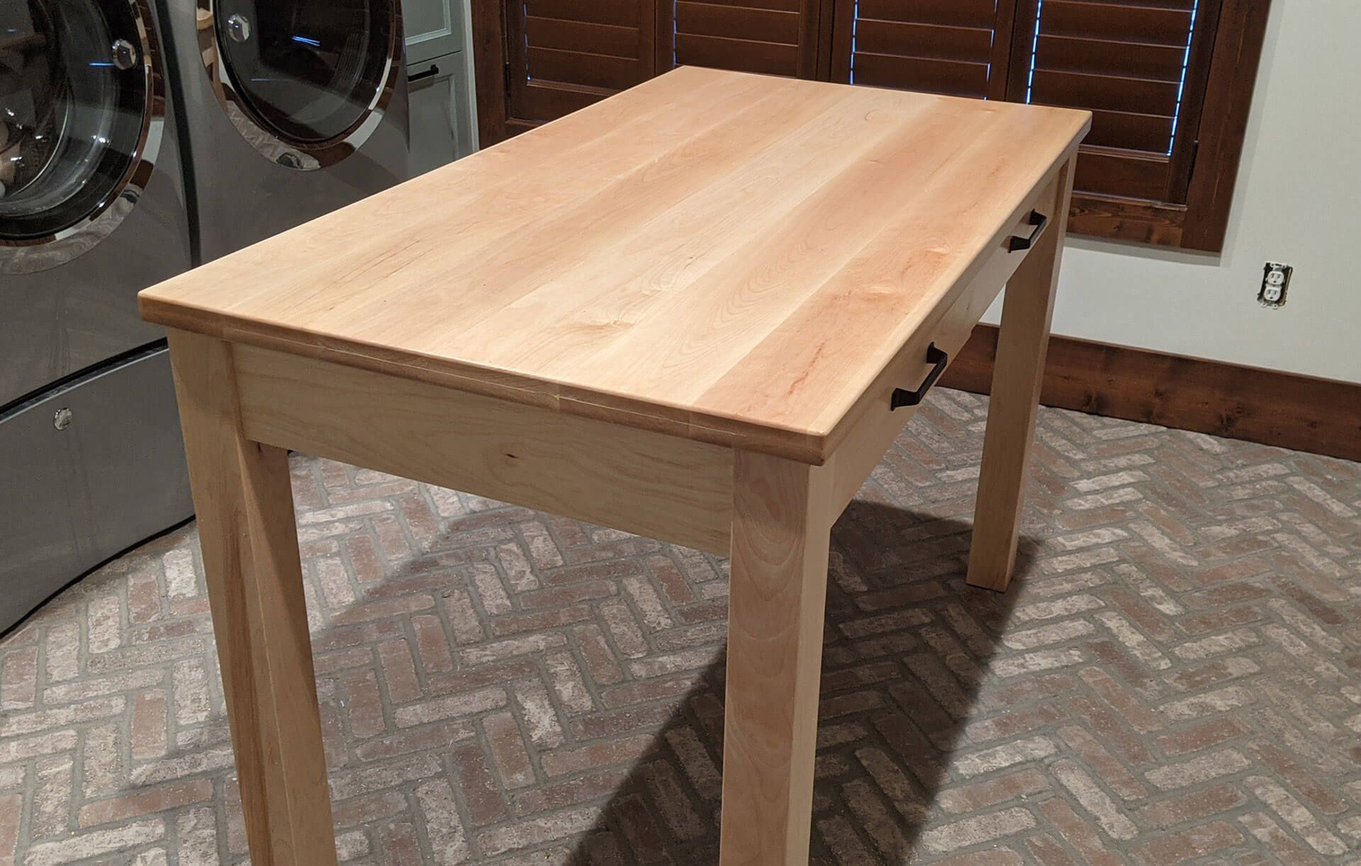 A wooden table is sitting in a laundry room next to a washer and dryer.