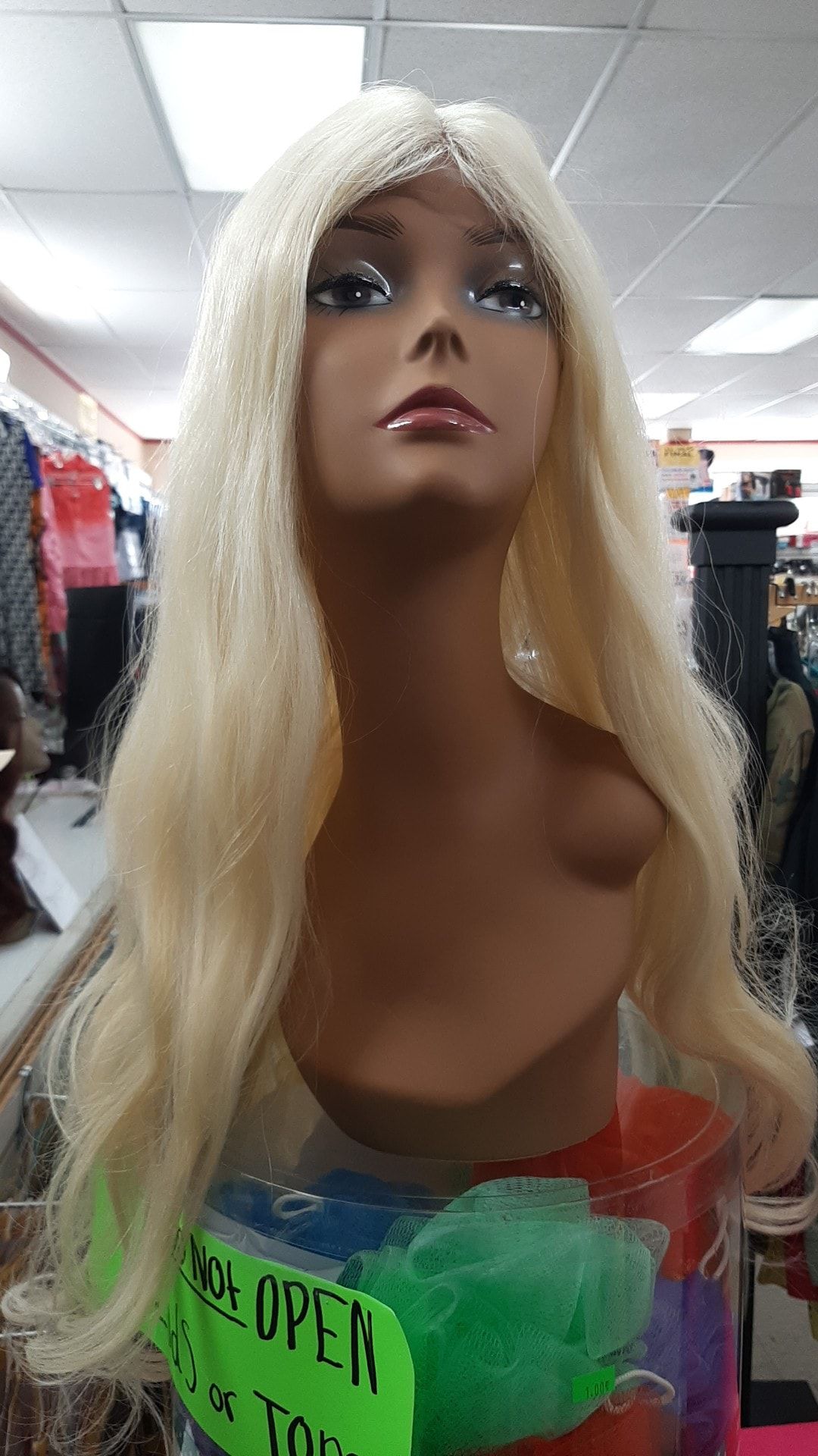 Mannequin head wearing a long, wavy, blonde wig, displayed in a shop.