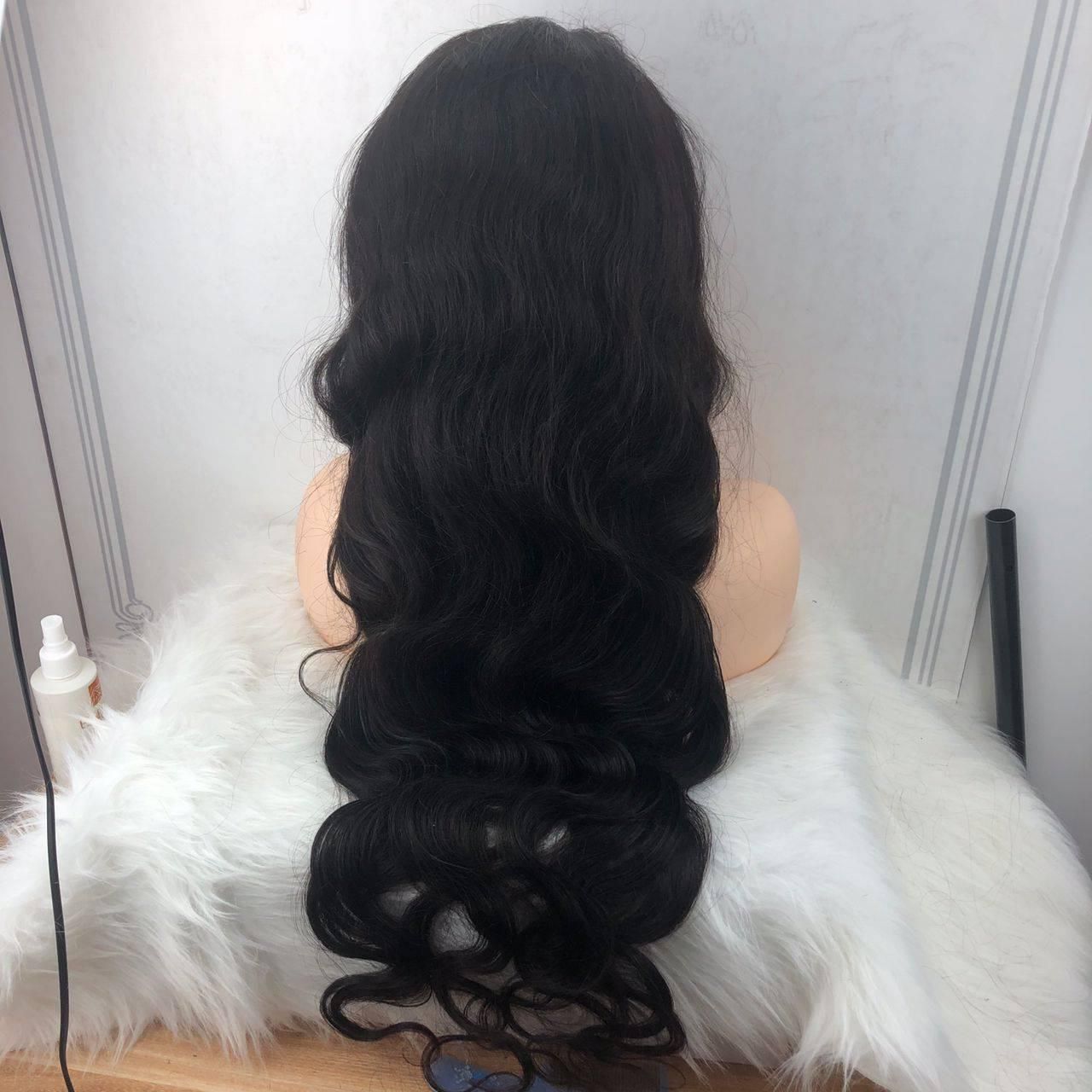 Black wavy wig on a mannequin head, resting on white fluffy fabric.