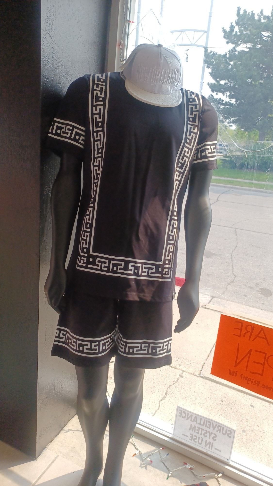 Mannequin wearing a black two-piece outfit with white greek key detailing; in a store window.