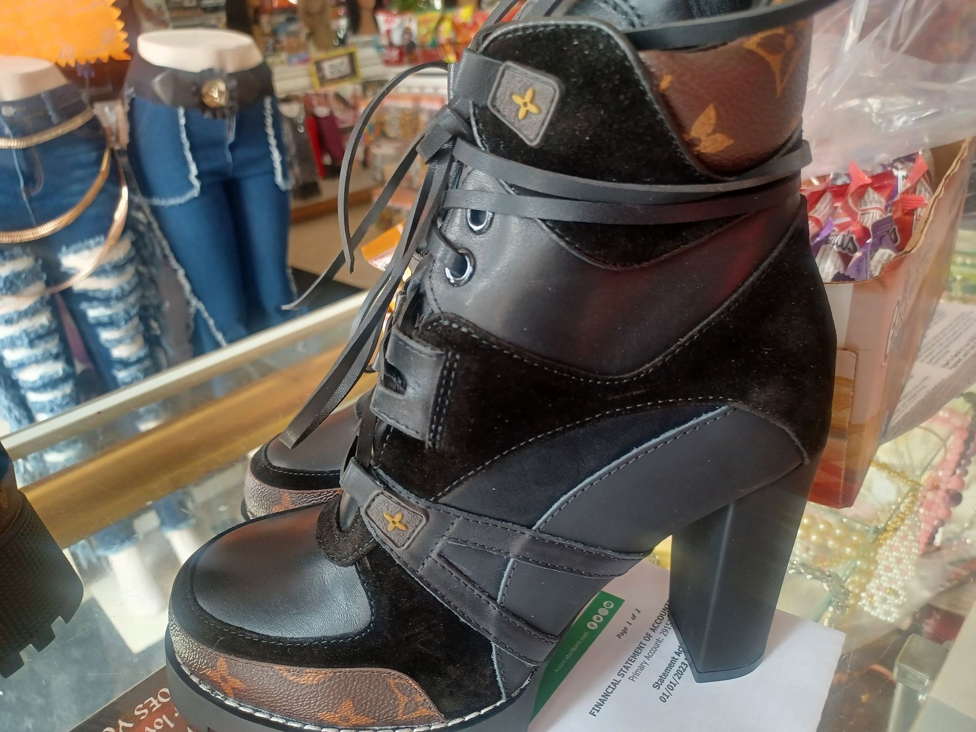 Black high-heeled combat boot with laces and a platform sole. Suede and leather details, on display in a store.