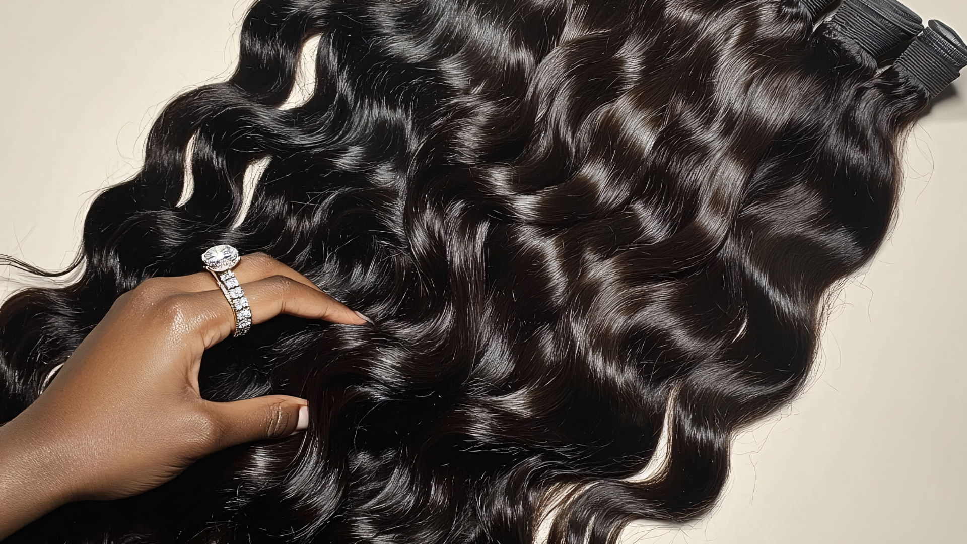 Hand touching wavy, black hair extensions with a silver ring on the finger.
