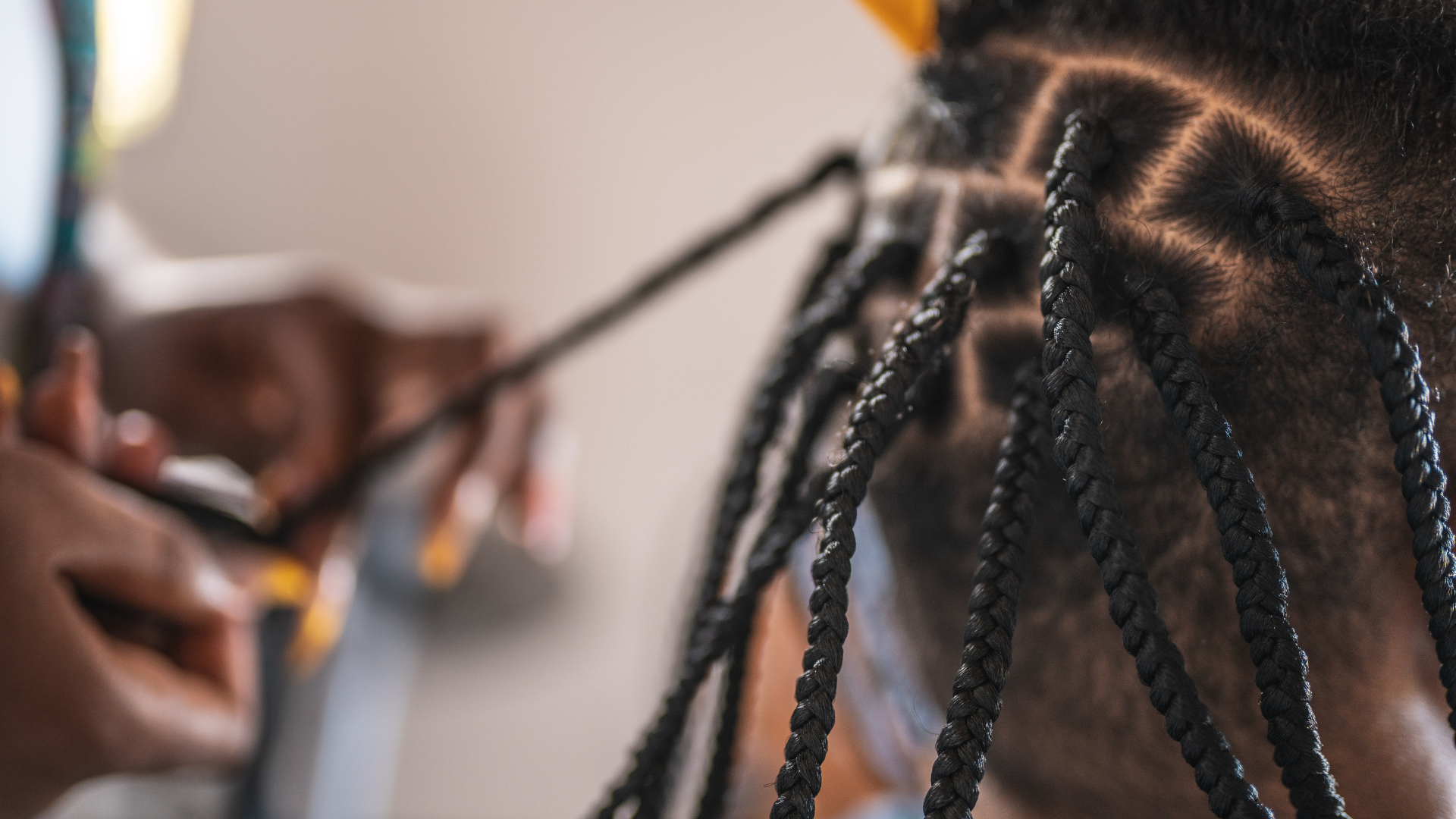 Hands braiding black hair, close up. Braids are being created in a geometric pattern.