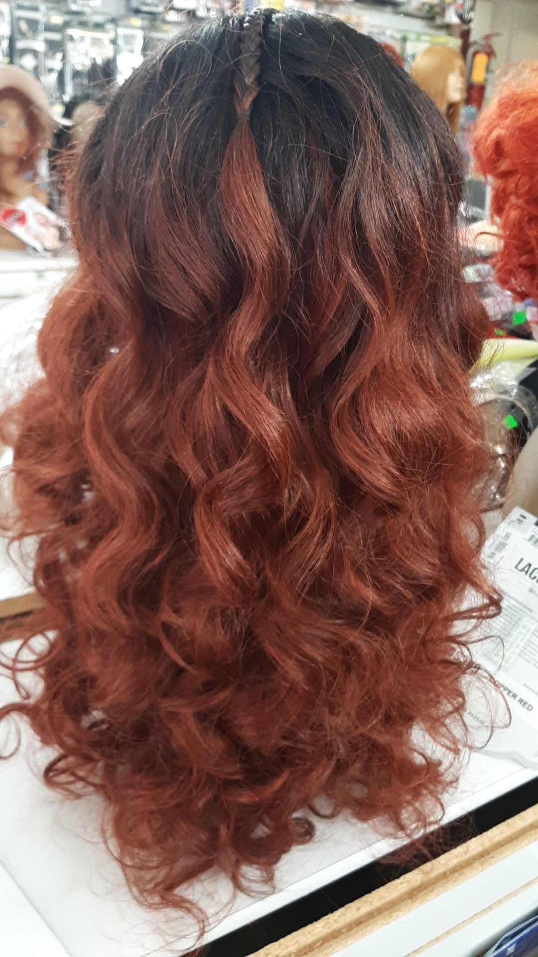 Wig with dark roots and auburn curls on display in a store.