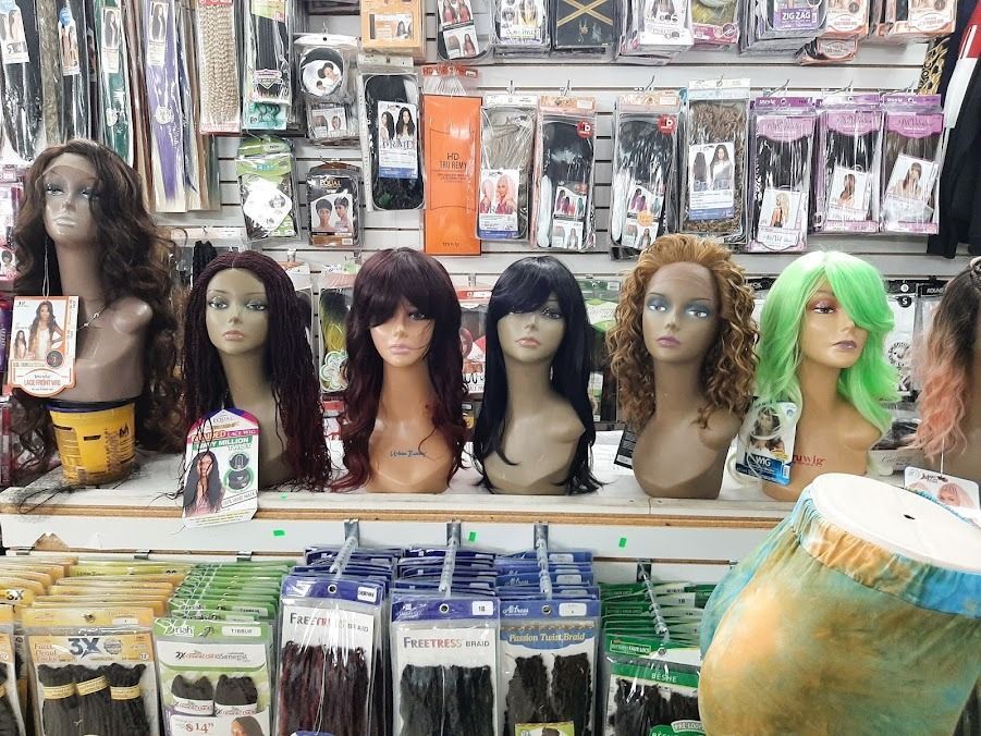 Wigs displayed on mannequin heads in a shop. Variety of colors and styles, with hair extensions below.