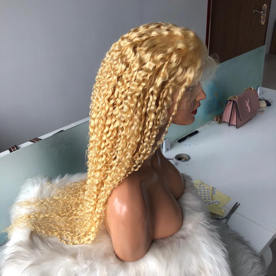 Blonde curly wig on a mannequin head, resting on a fluffy white surface; desk in the background.