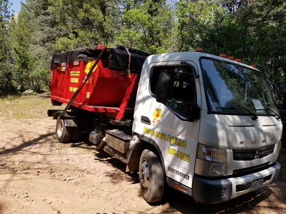 A dump truck with a red dumpster attached to it is parked in a dirt lot.
