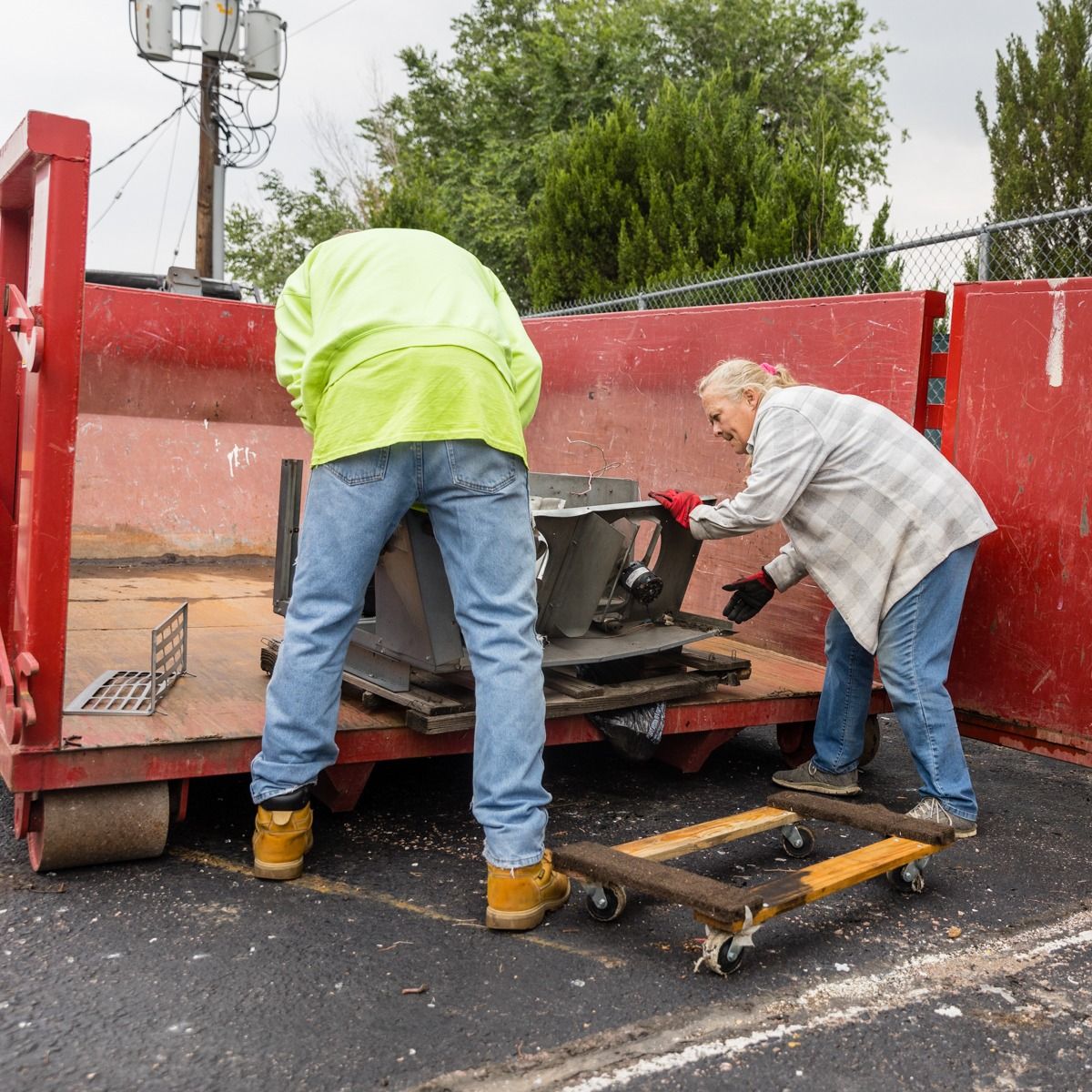 A man and a woman are loading a red dumpster