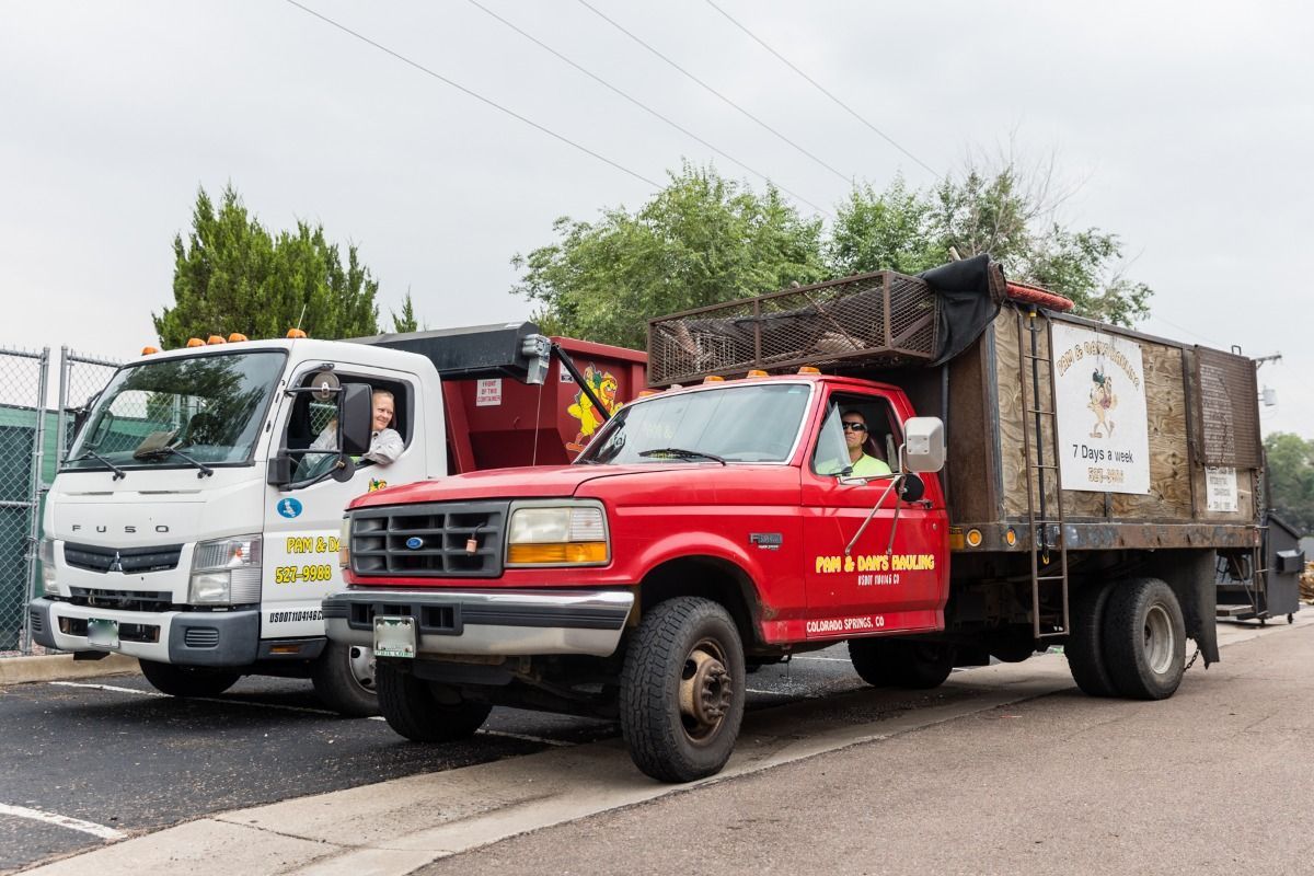 Two garbage trucks are parked next to each other on the side of the road.