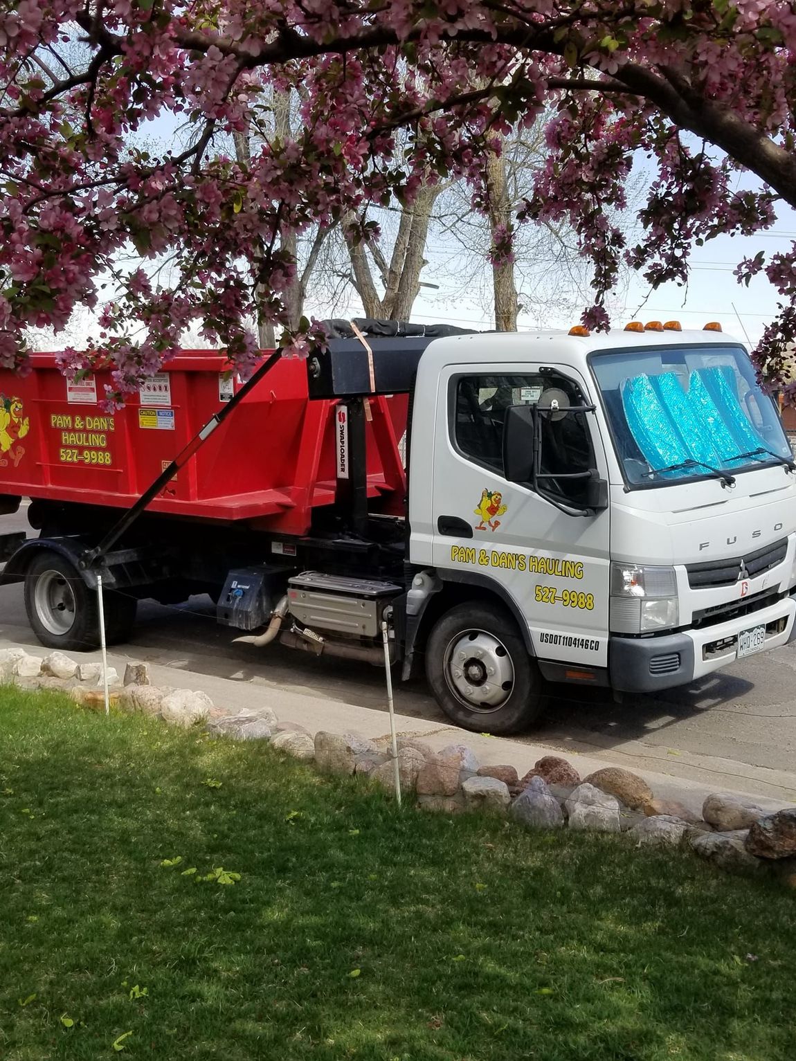 A dump truck is parked in front of a cherry blossom tree.