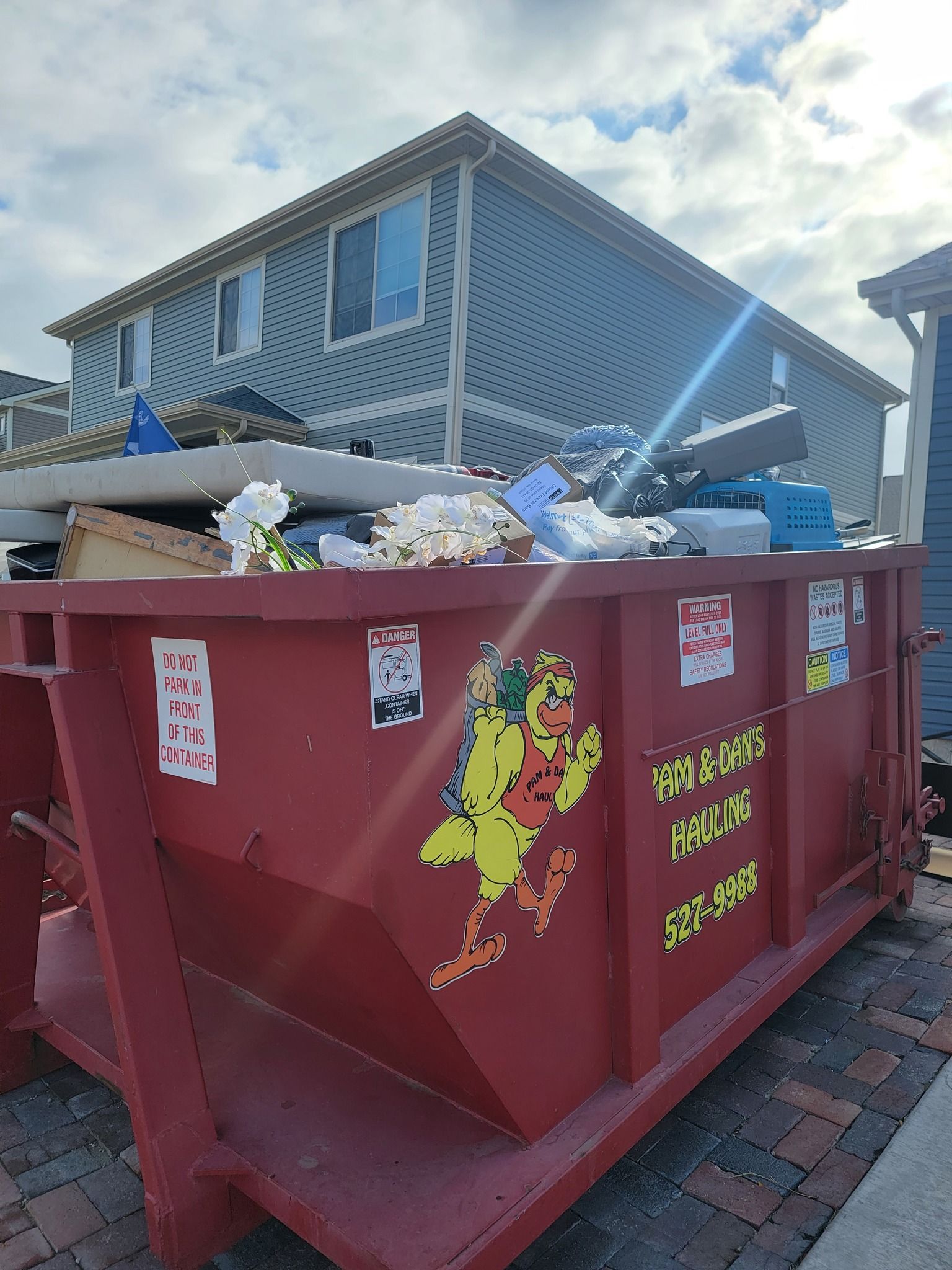 A large red dumpster is sitting in front of a house.