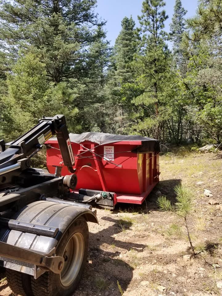 A man in a green shirt is loading a trash can into a garbage truck