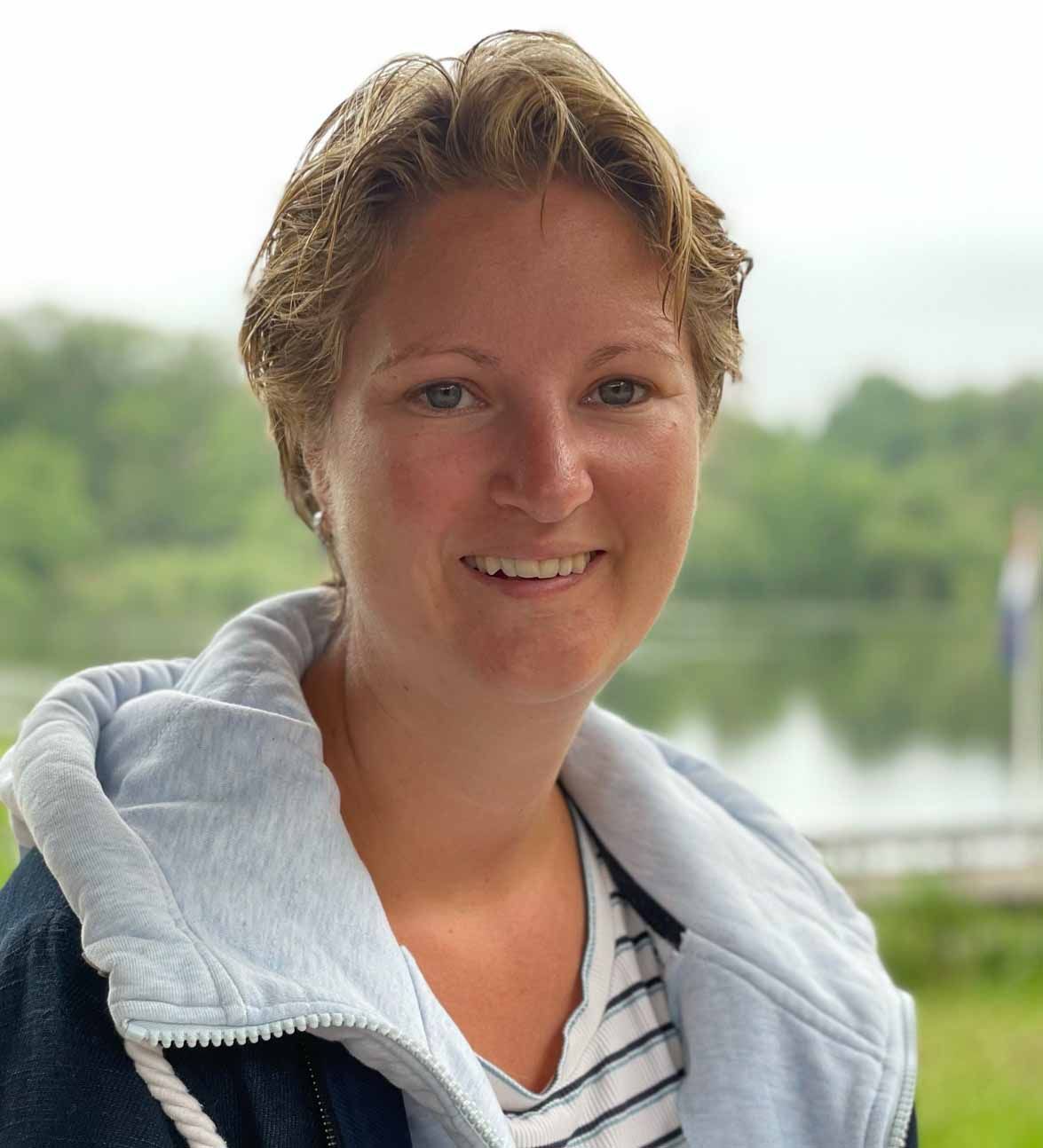 Een vrouw in een gestreept shirt en een blauw jasje lacht naar de camera