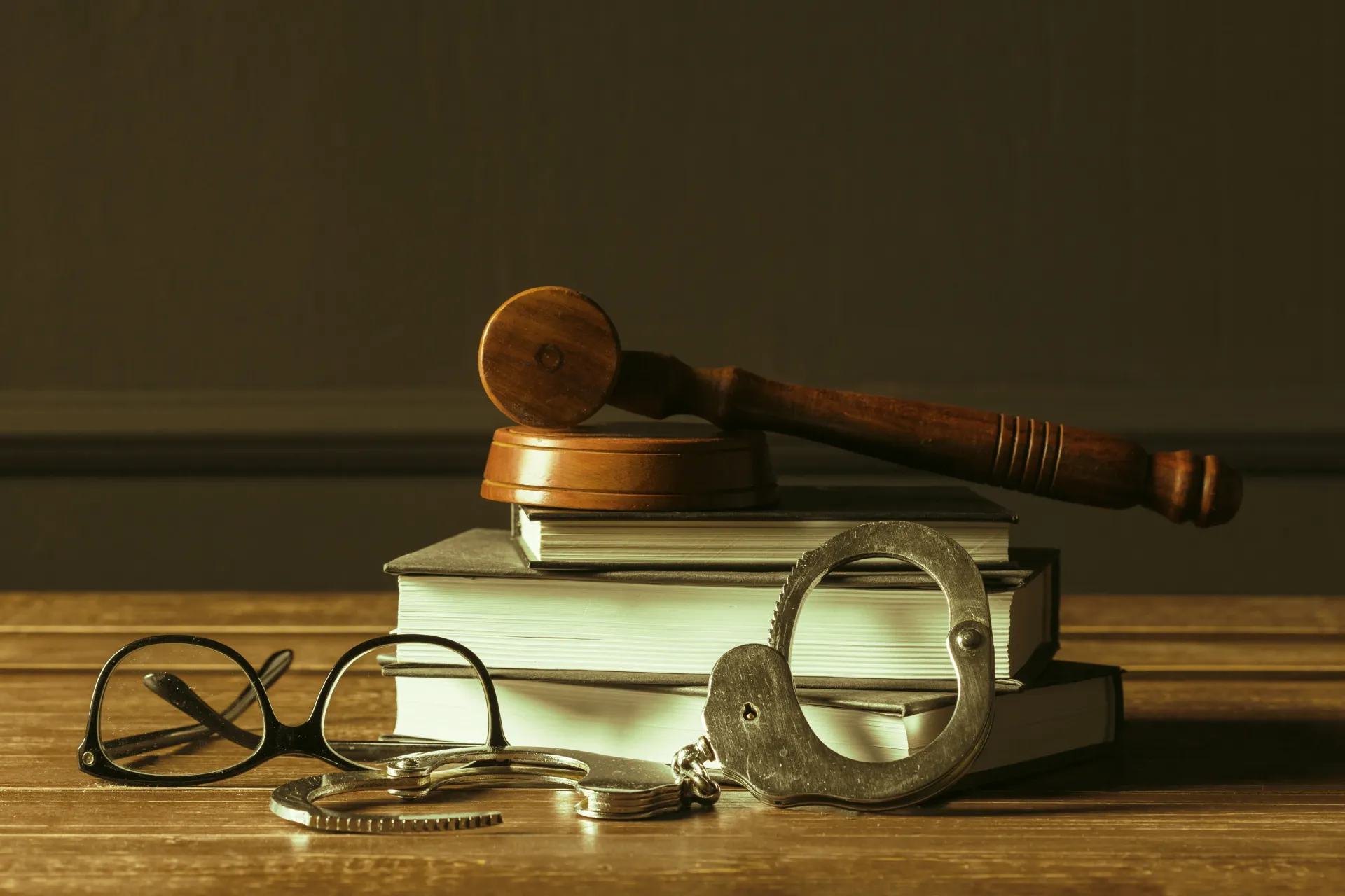 Law books with a gavel, eyeglasses, and a handcuff on a wooden desk