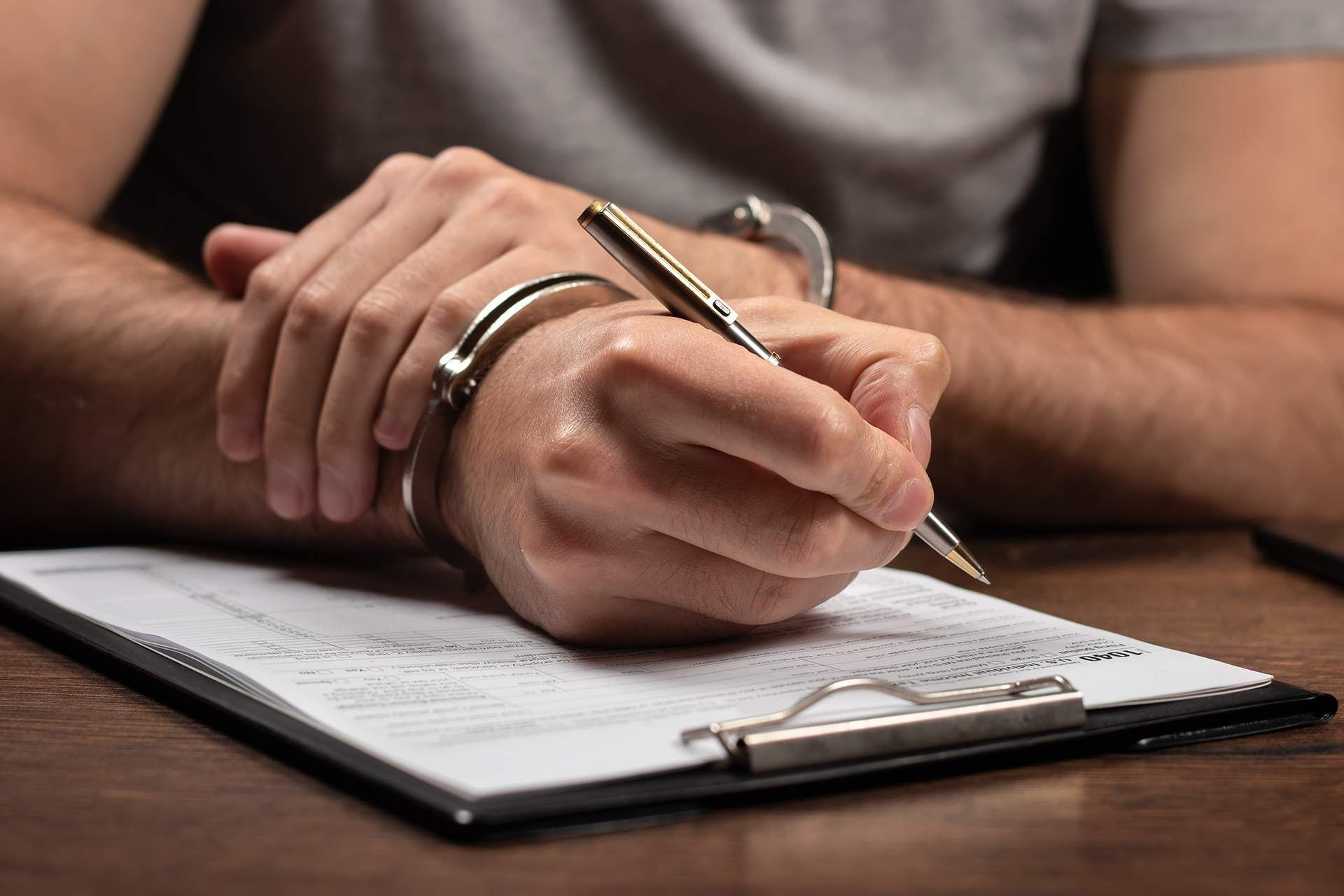 Person in handcuffs writing on a clipboard with a pen.