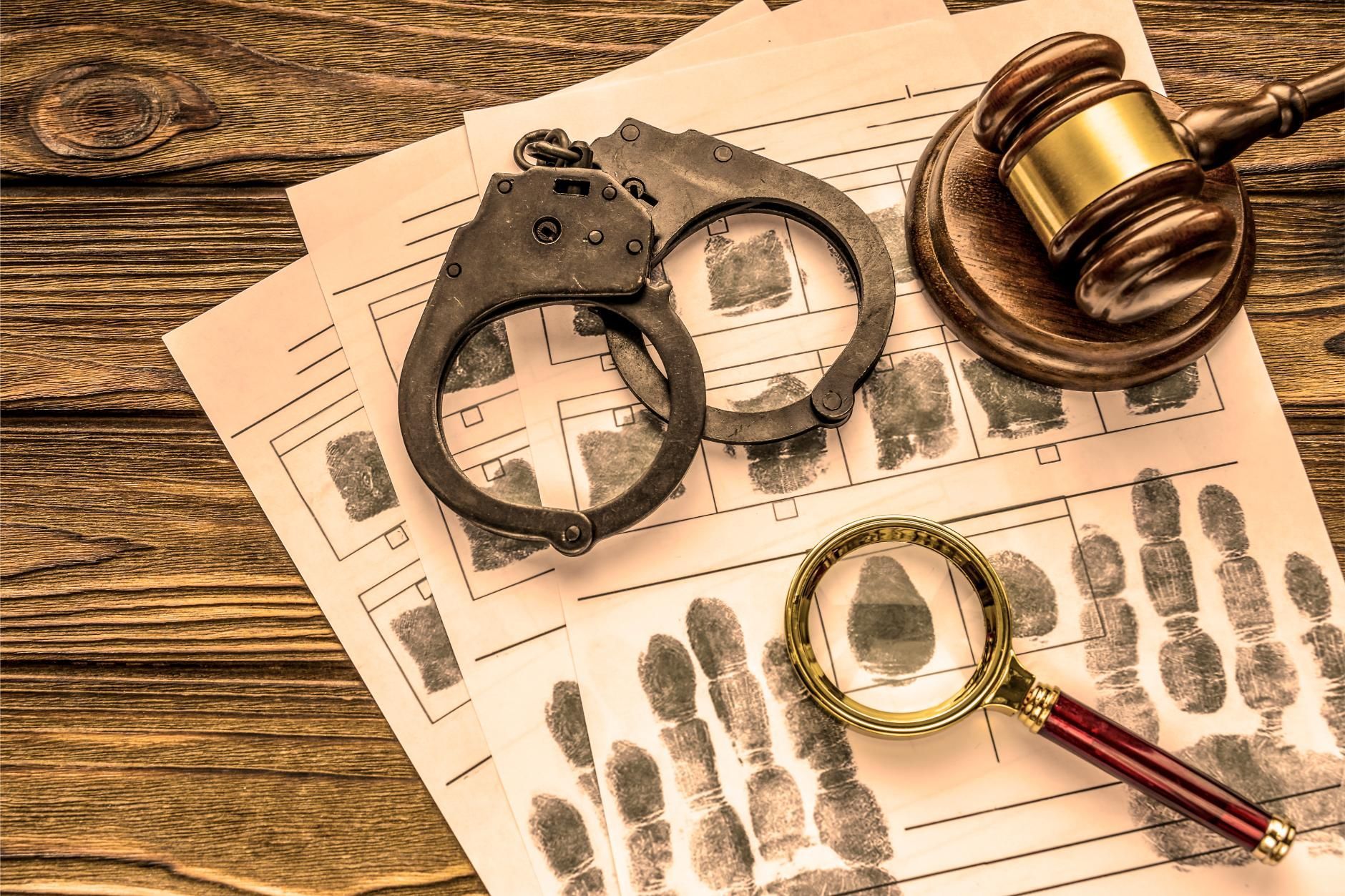 Handcuffs, magnifying glass, and gavel on fingerprint evidence sheets, likely at a crime scene.