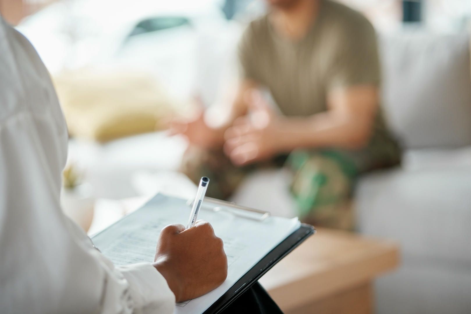 Therapist taking notes during a consultation with a person in military uniform. Interior setting.