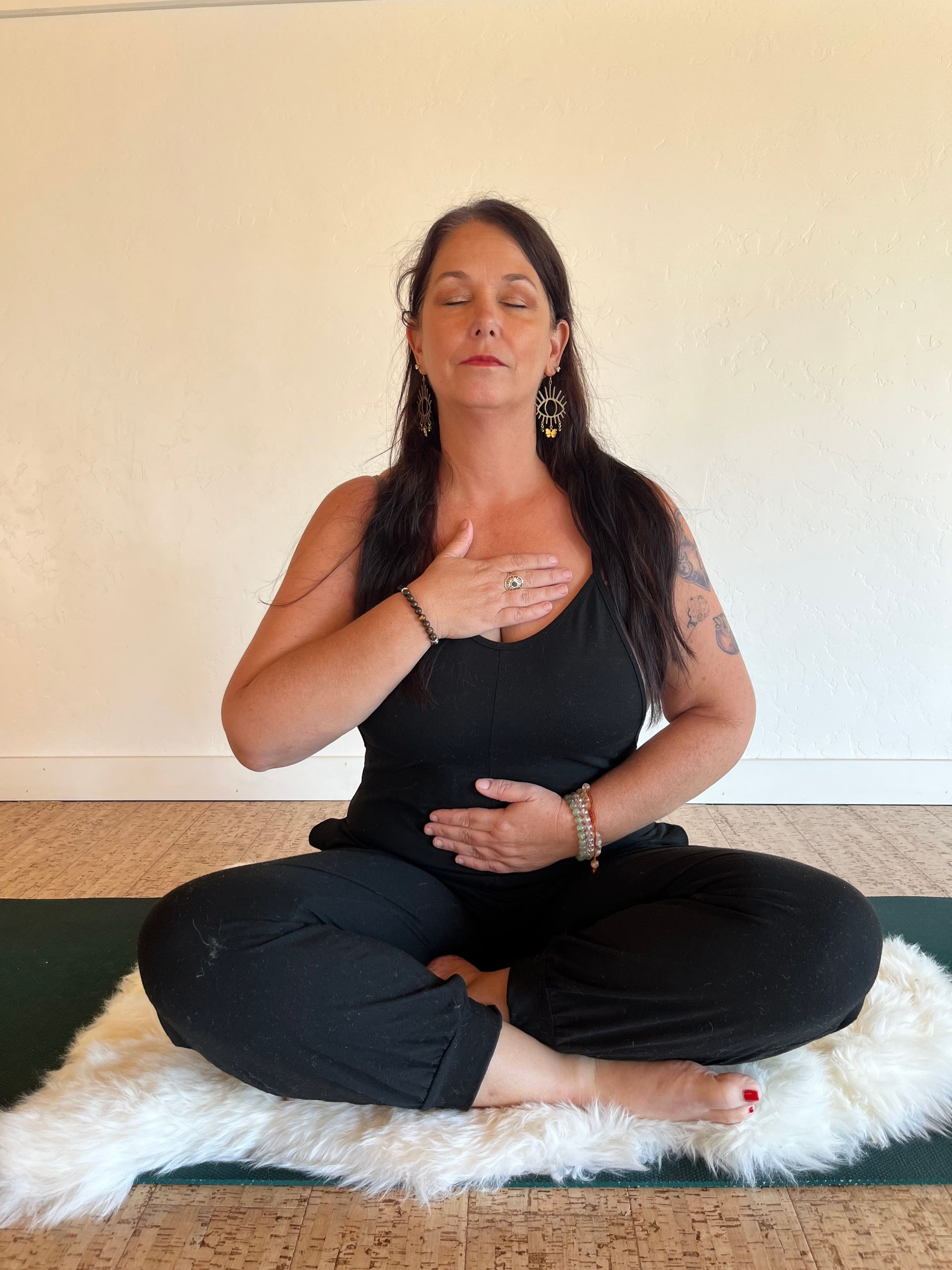 Woman in black outfit meditating with hands on chest and stomach, eyes closed.