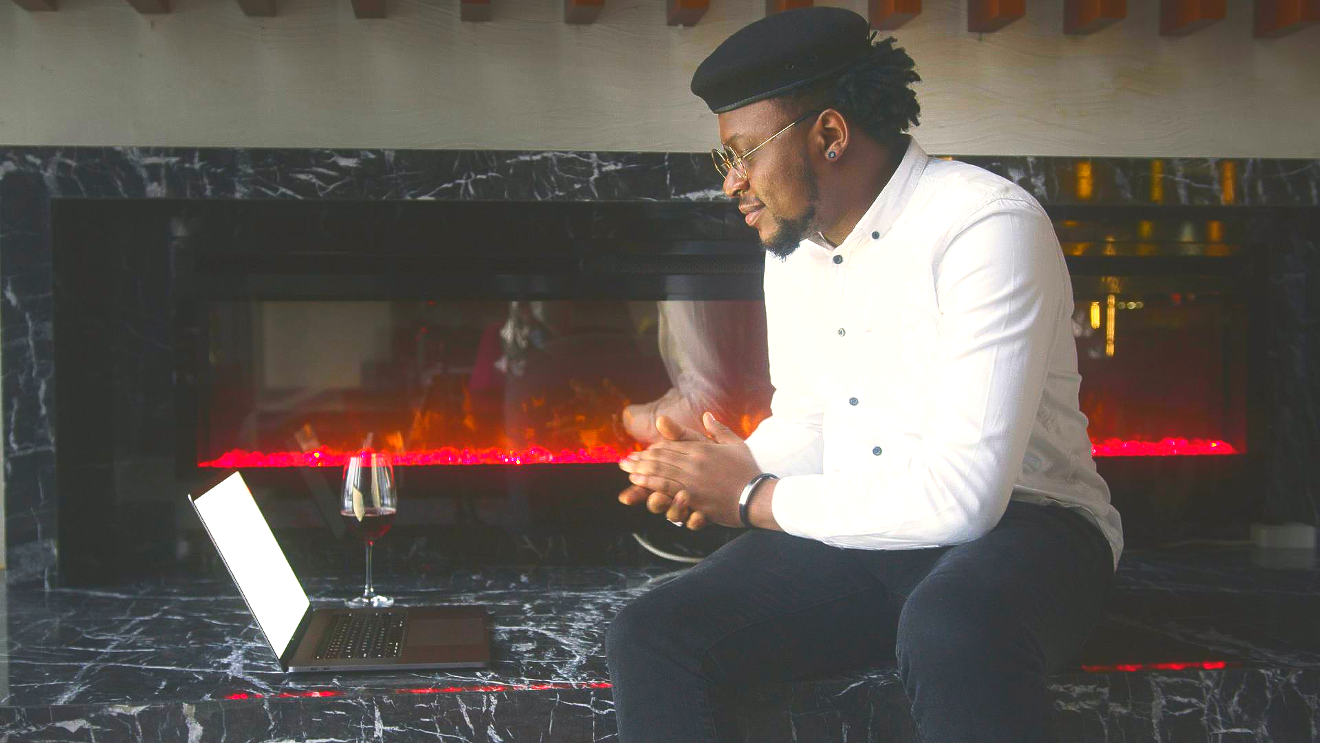 Man in white shirt and glasses in front of laptop and fireplace.