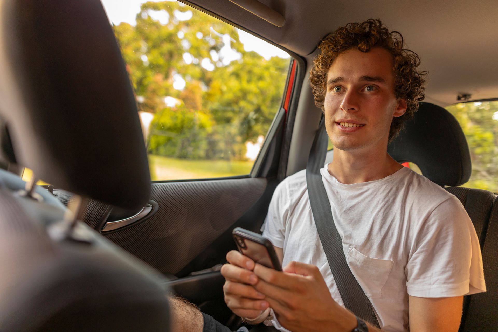 A young man is sitting in the back seat of a car looking at his cell phone.