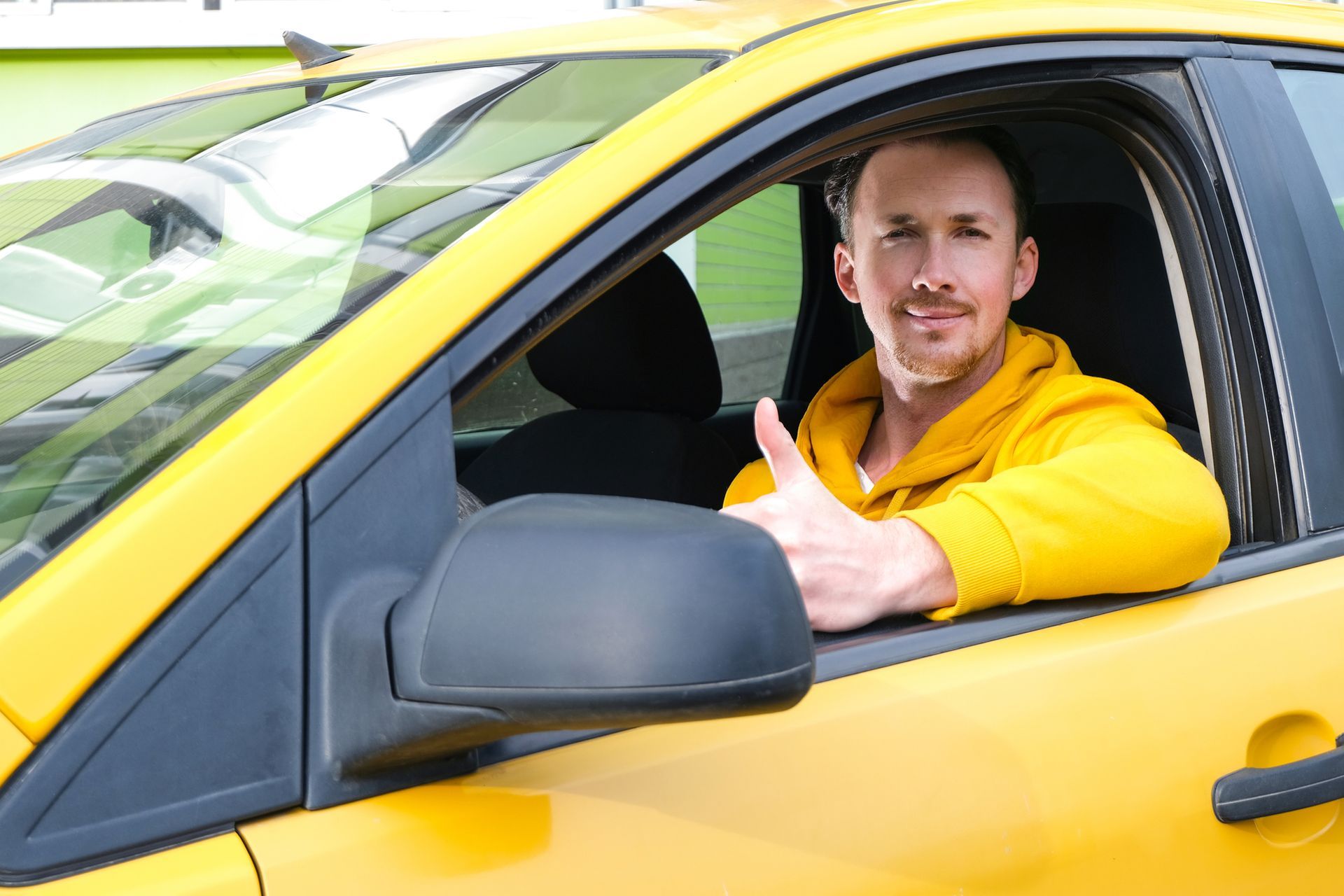 A man is sitting in a yellow car giving a thumbs up.