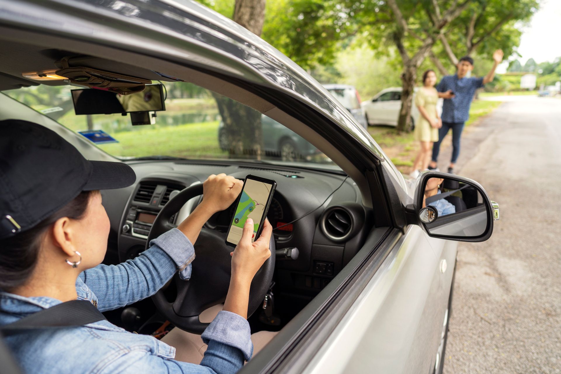 A woman is driving a car and using a tablet.