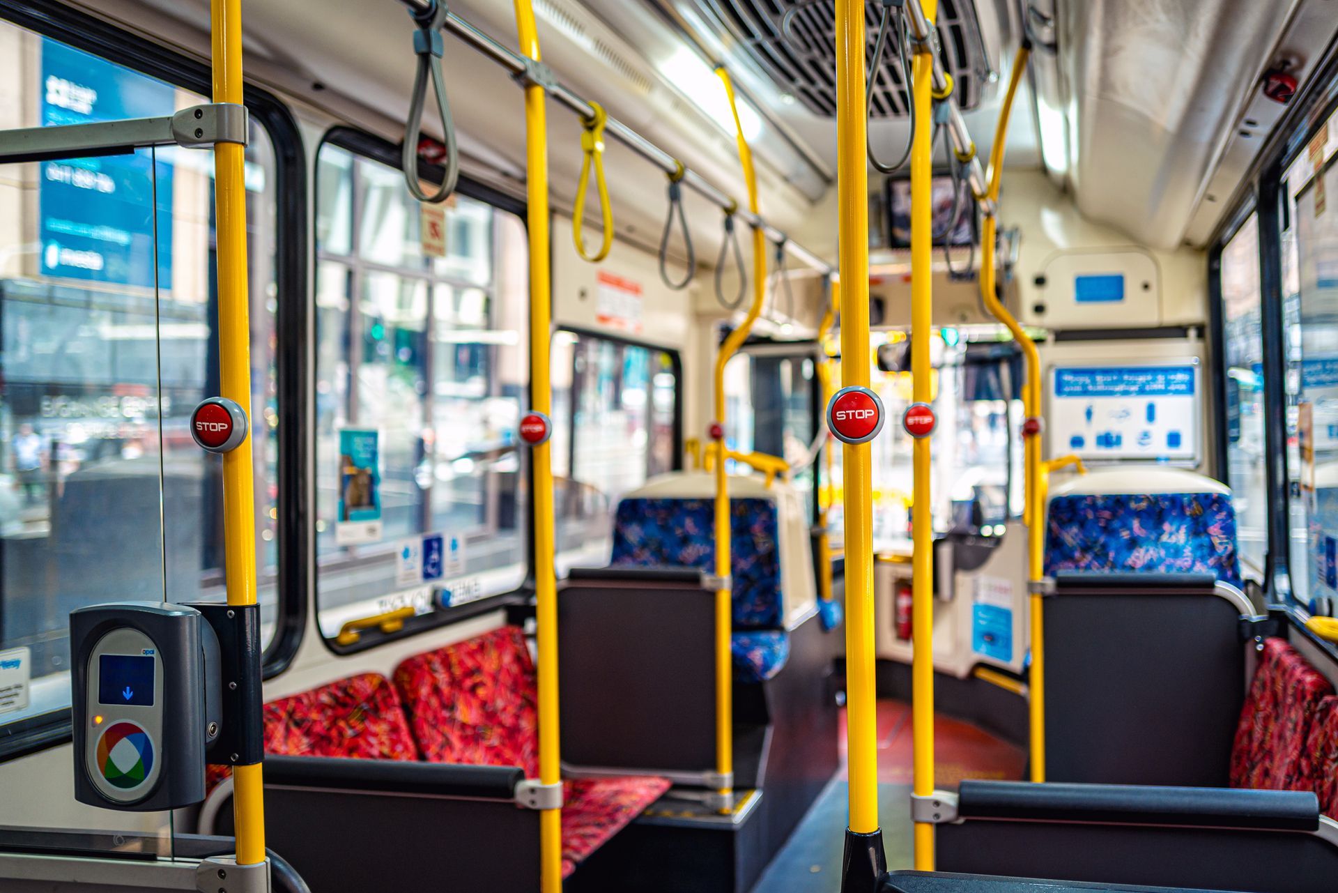 The inside of an empty bus with red seats and yellow poles.