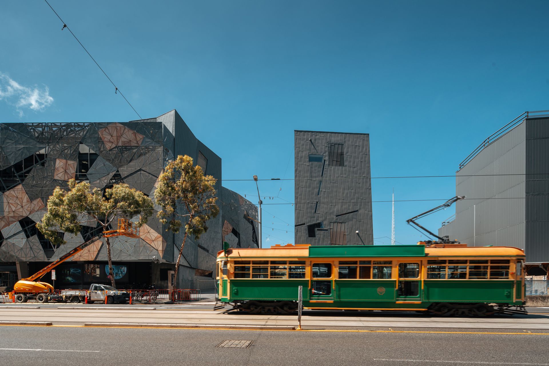 A green and yellow trolley is driving down the street in front of a building.