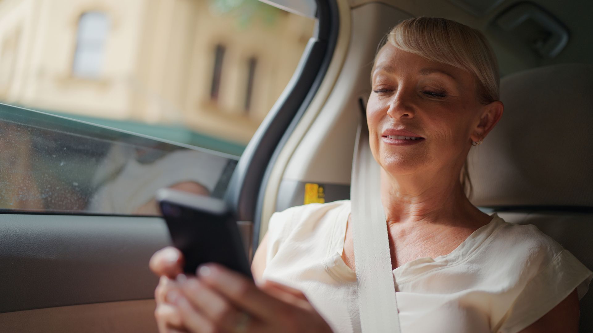 A woman is sitting in the back seat of a car looking at her cell phone.