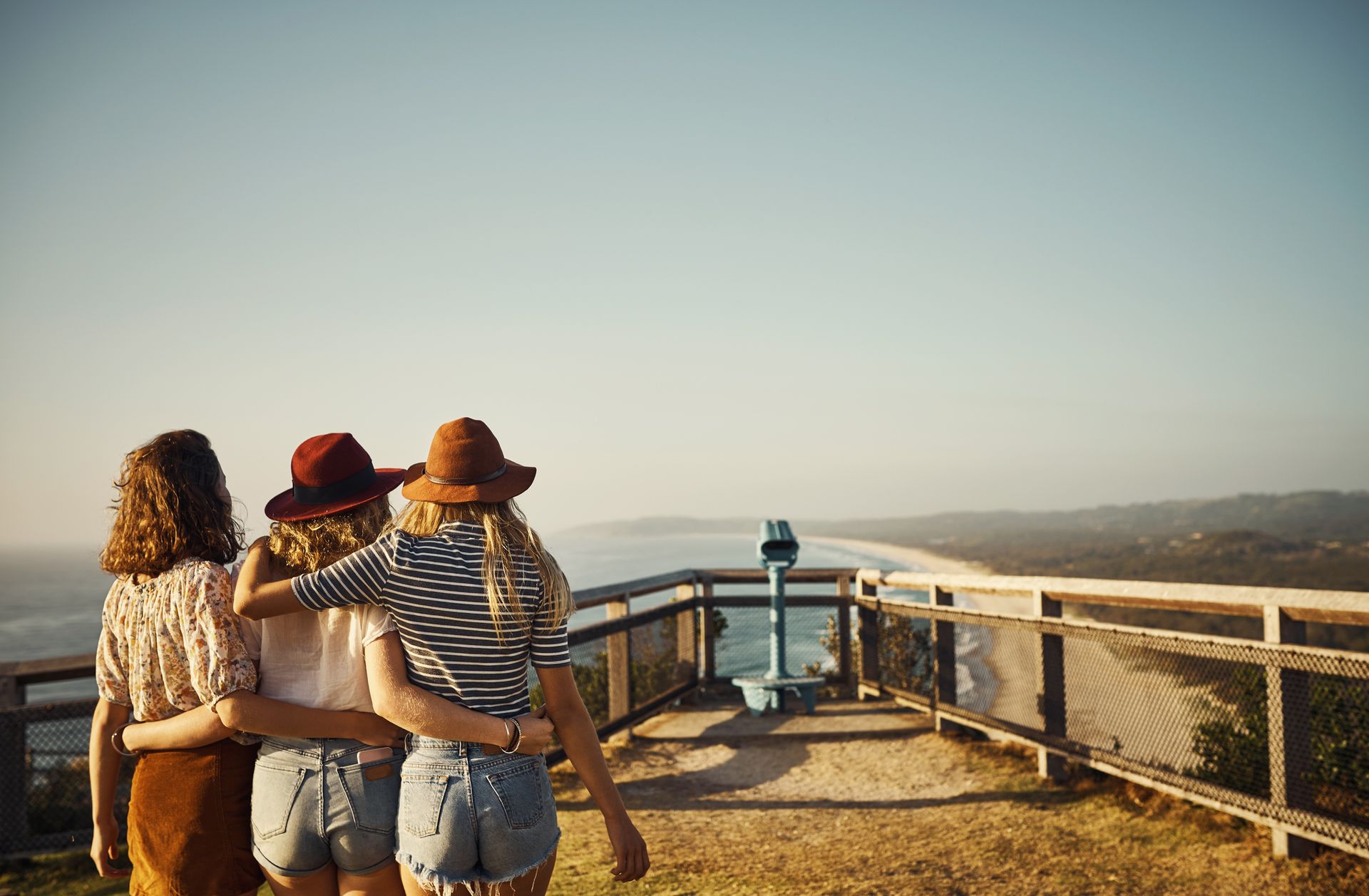Three women are standing on top of a hill looking at the ocean.