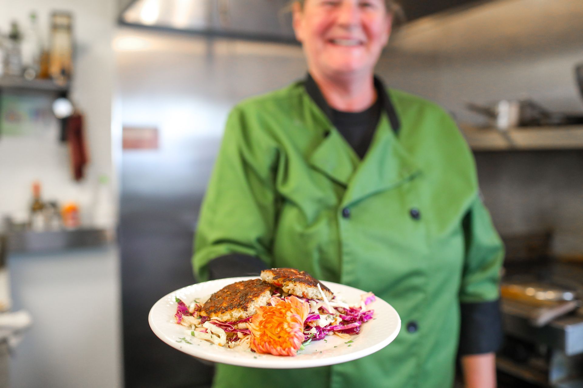 A woman in a green jacket is holding a plate of food.