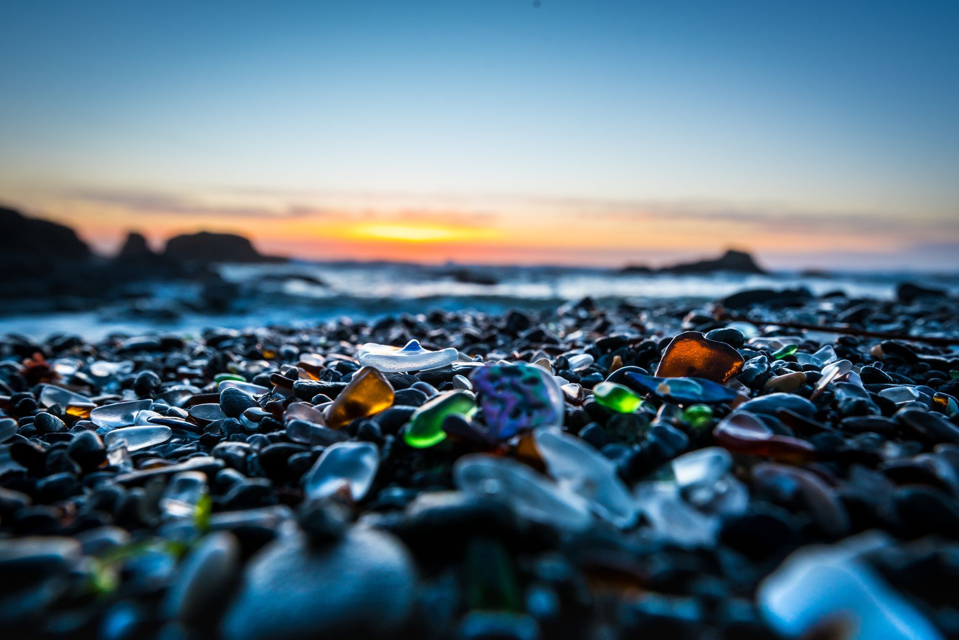 A pile of glass rocks on a beach with a sunset in the background.