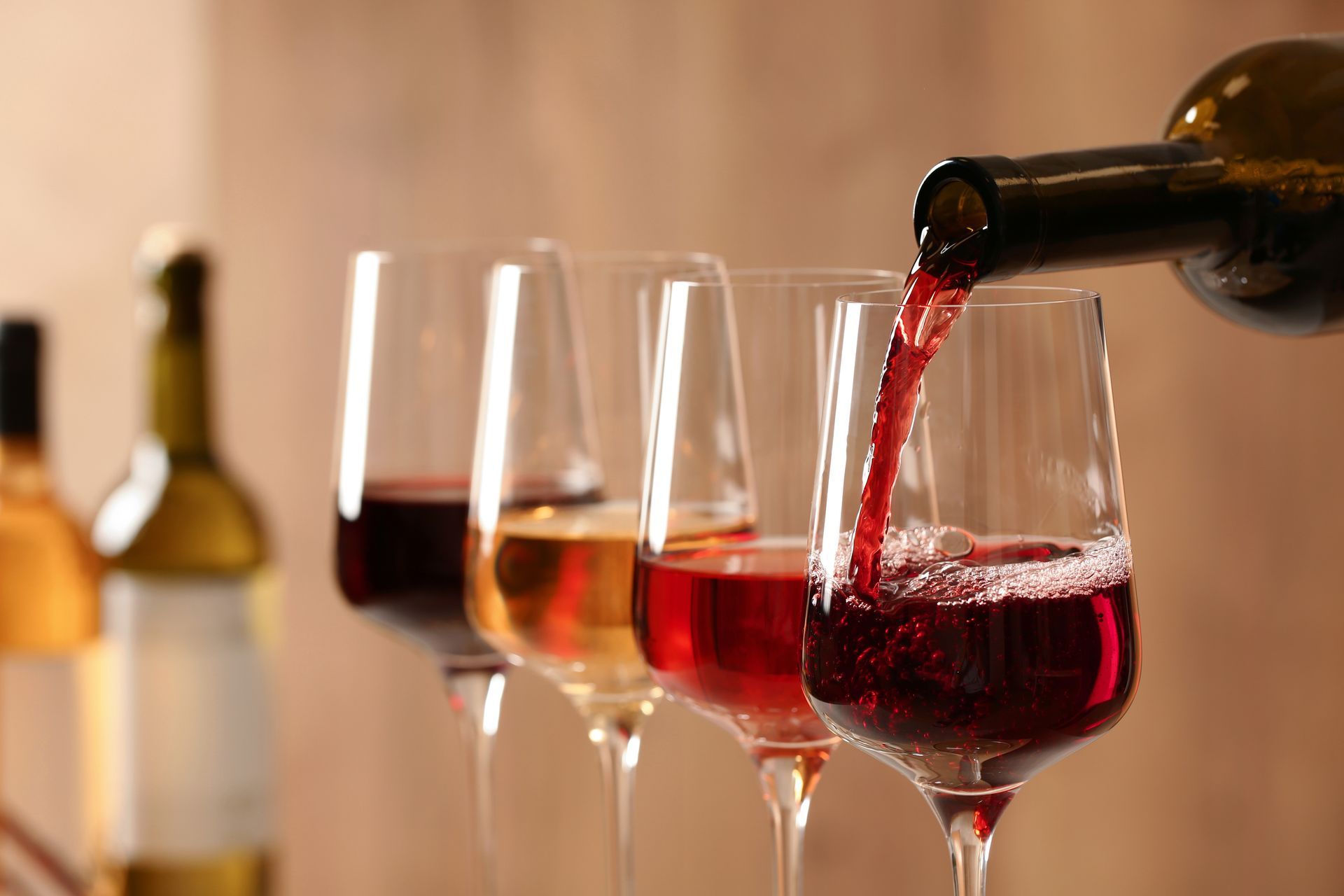 A bottle of wine is being poured into a row of wine glasses.